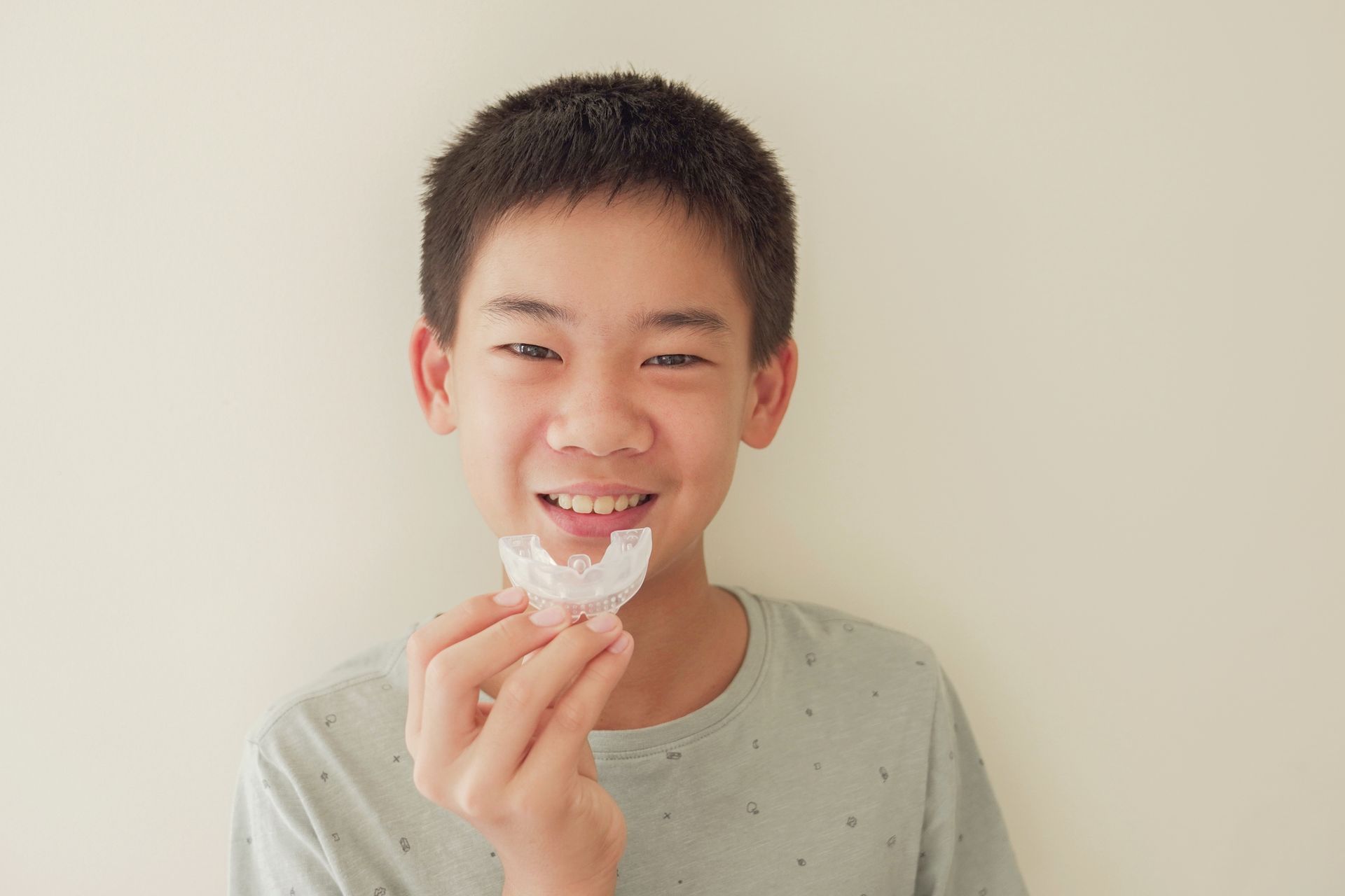 A young boy is holding a mouth guard in his hand and smiling.