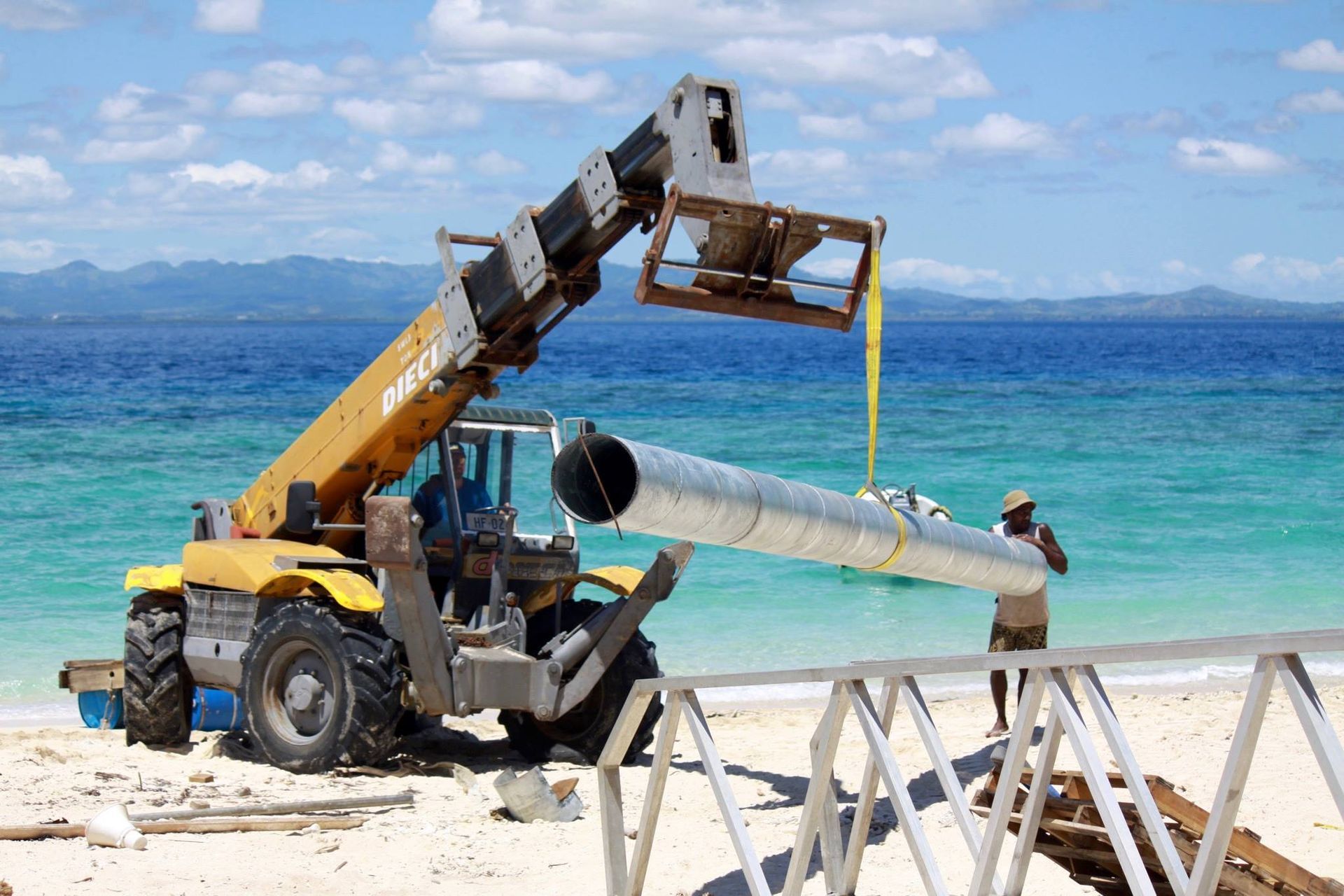 a crane lifting pipes on a white sand beach by the ocean