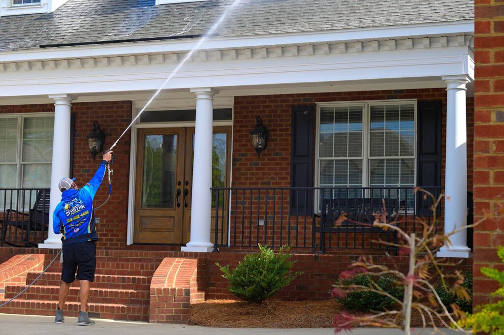 A man is cleaning the roof of a brick house with a high pressure washer.