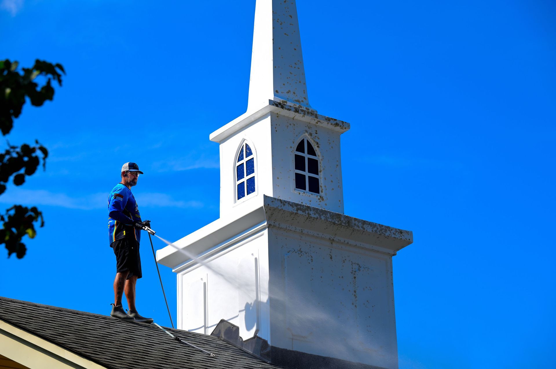 A man is cleaning the roof of a church with a high pressure washer.