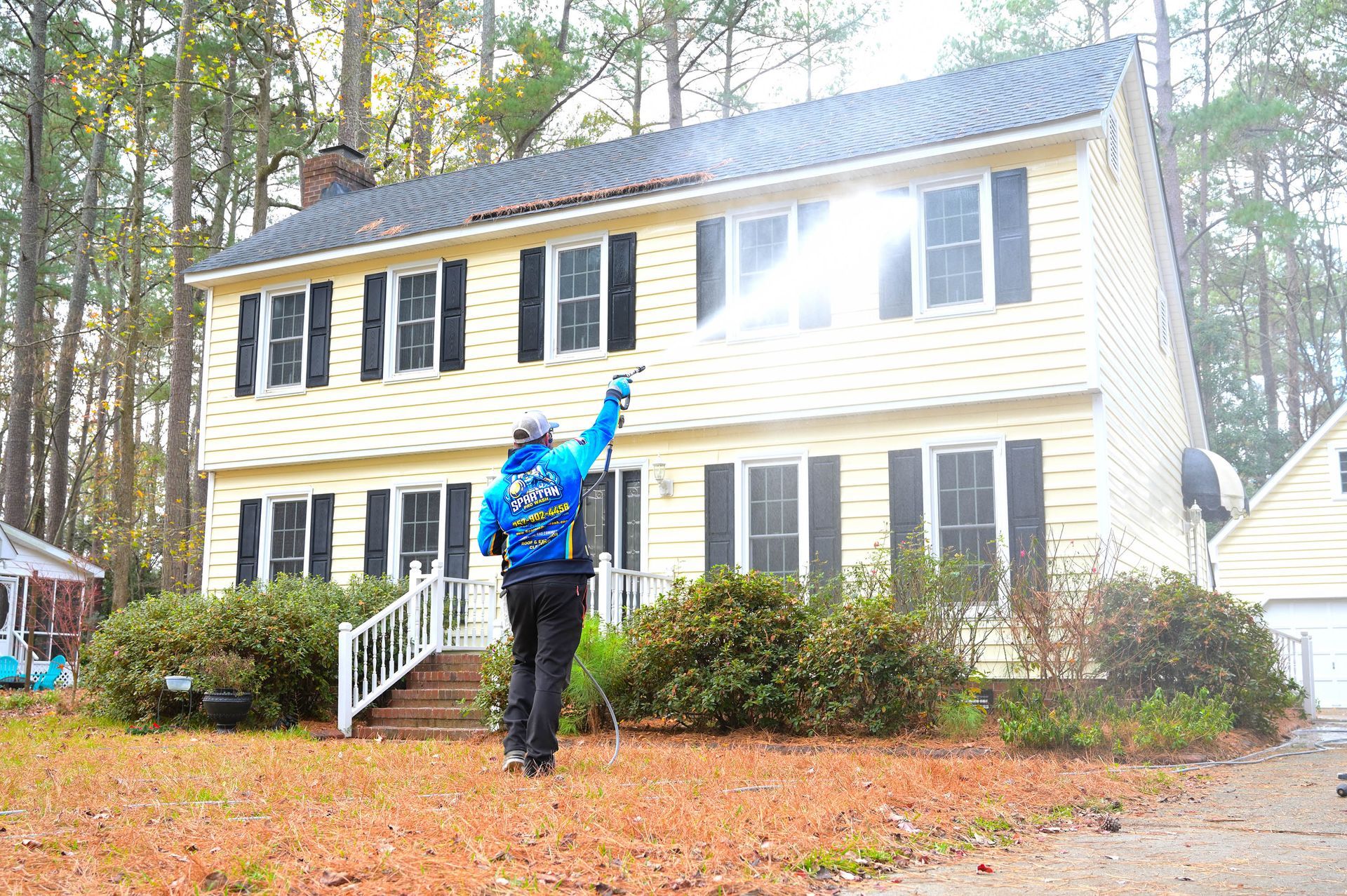 A man is cleaning the windows of a house with a pressure washer.