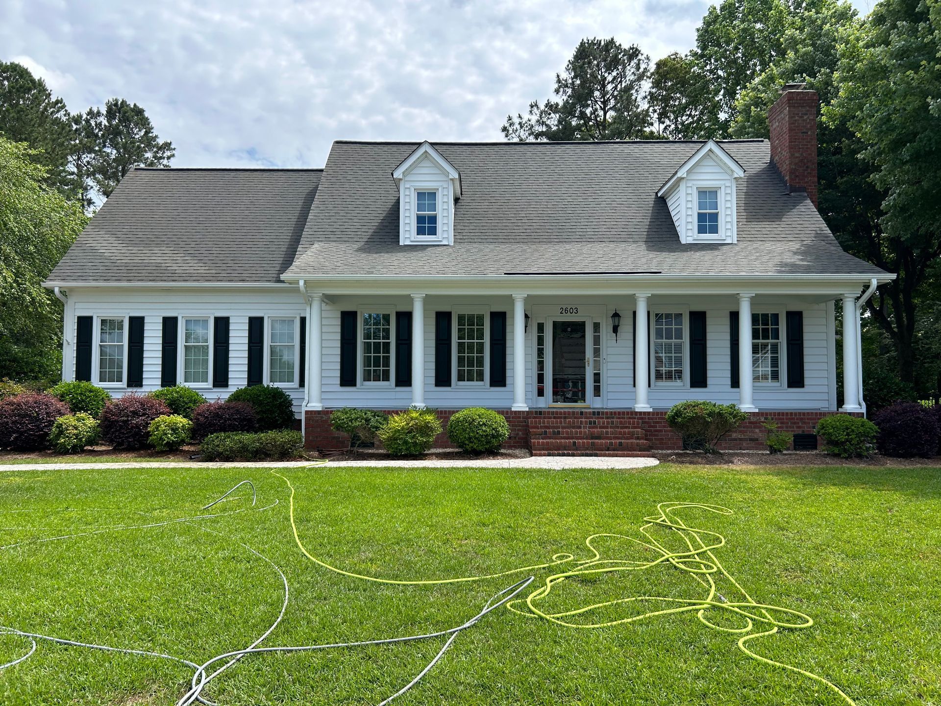 A man is standing on a ladder spraying water on a roof.