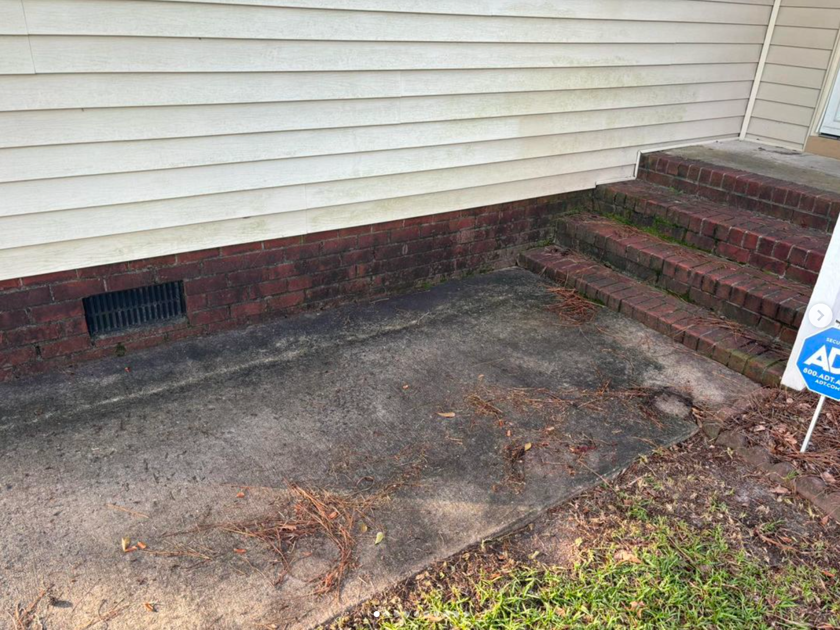 A dirty sidewalk in front of a house with a for sale sign.