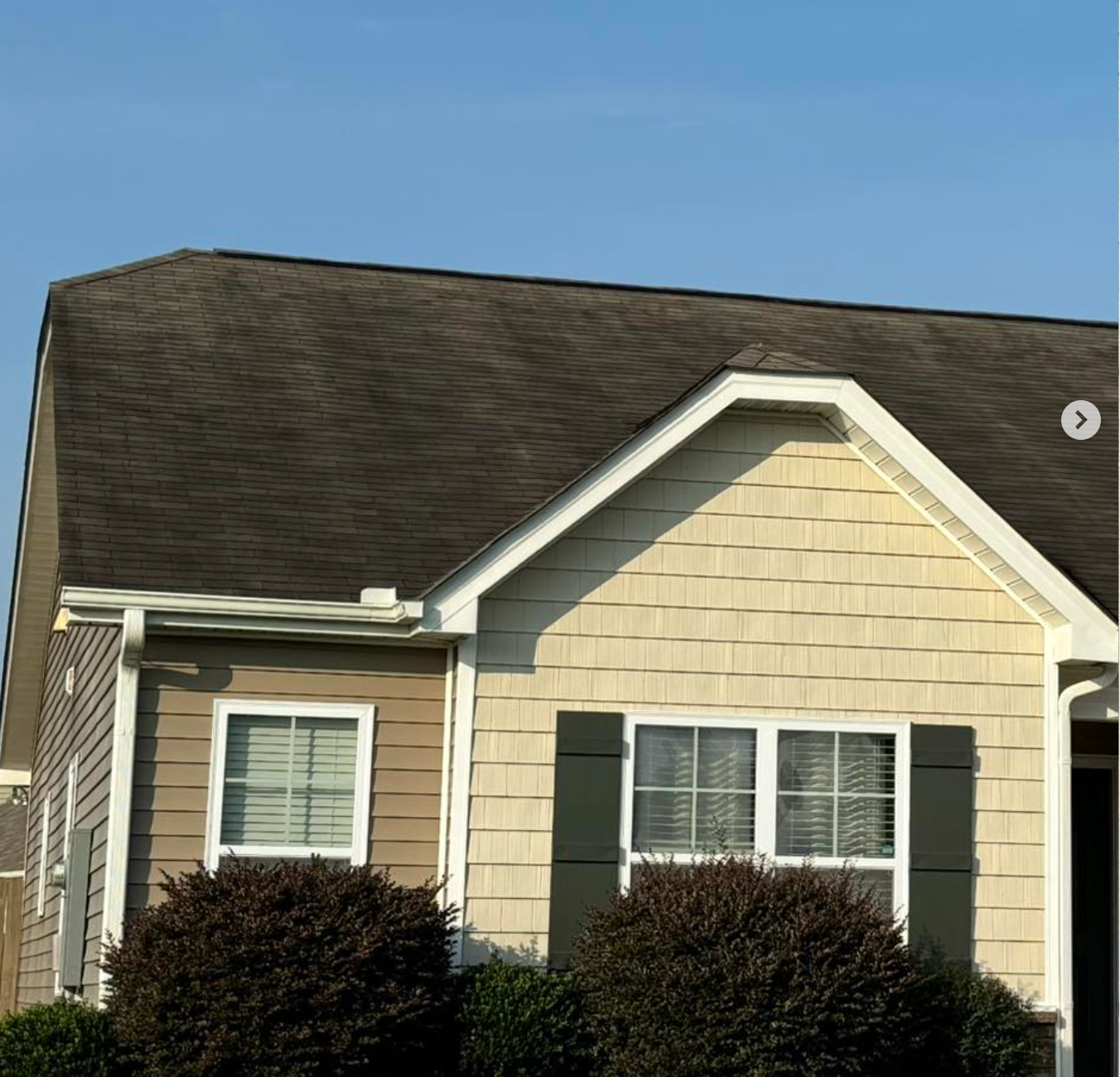 House exterior with tan siding, dark roof, and white-trimmed windows under a clear blue sky