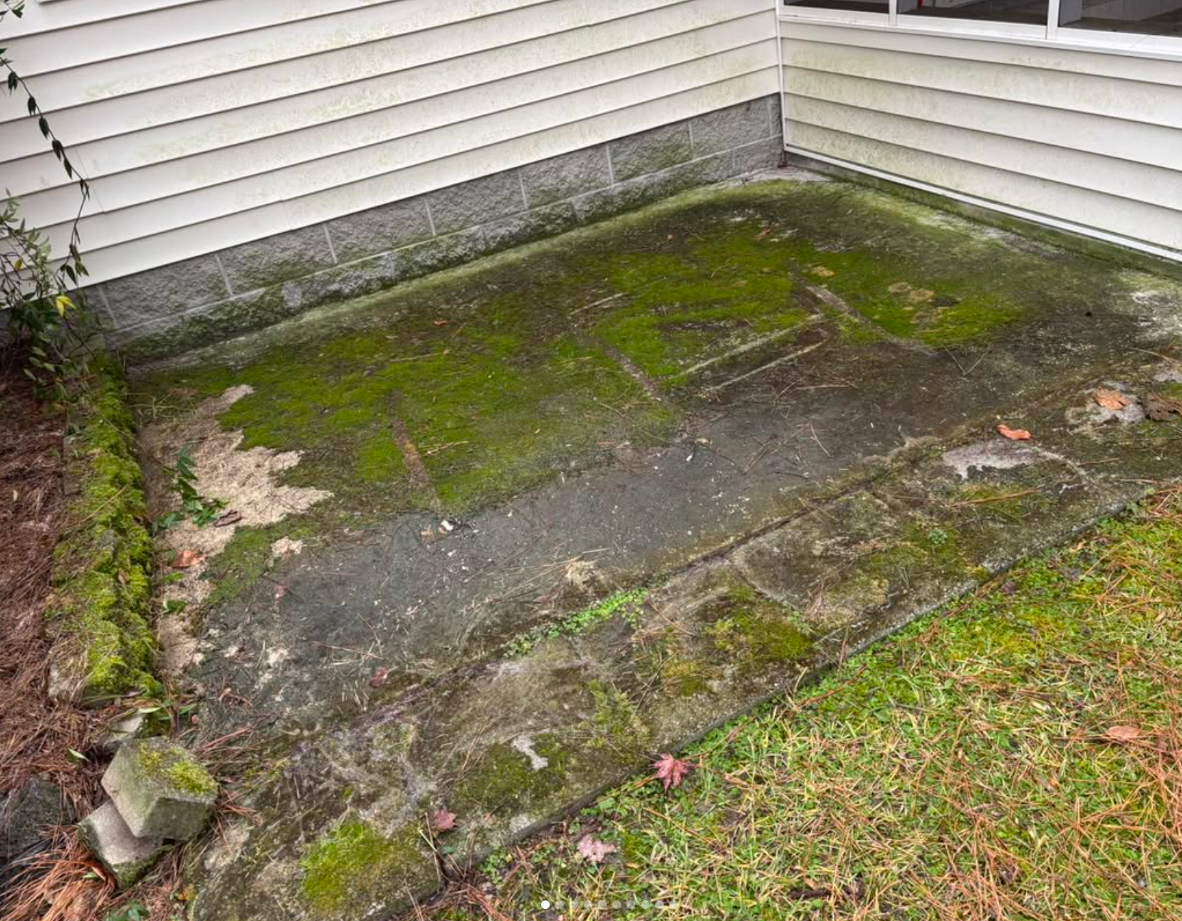 A dirty concrete patio with moss growing on it next to a house.