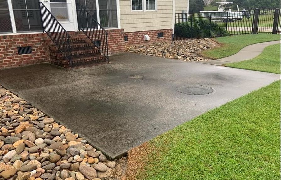 A concrete driveway in front of a brick house with stairs and a flag.