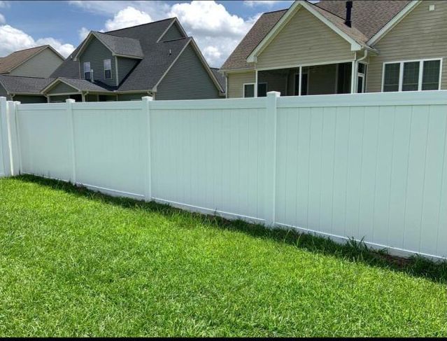 A white fence surrounds a lush green yard in front of a house.