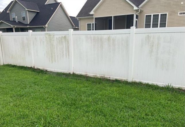 A white fence surrounds a lush green lawn in front of a house.