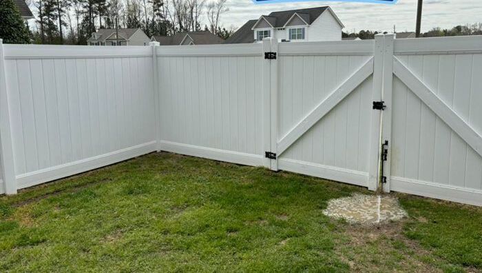 A white fence with a gate in the backyard of a house.