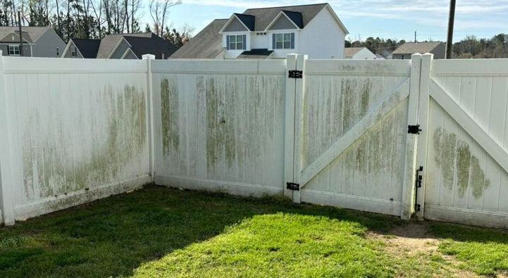 A dirty white fence with a gate in the backyard of a house.