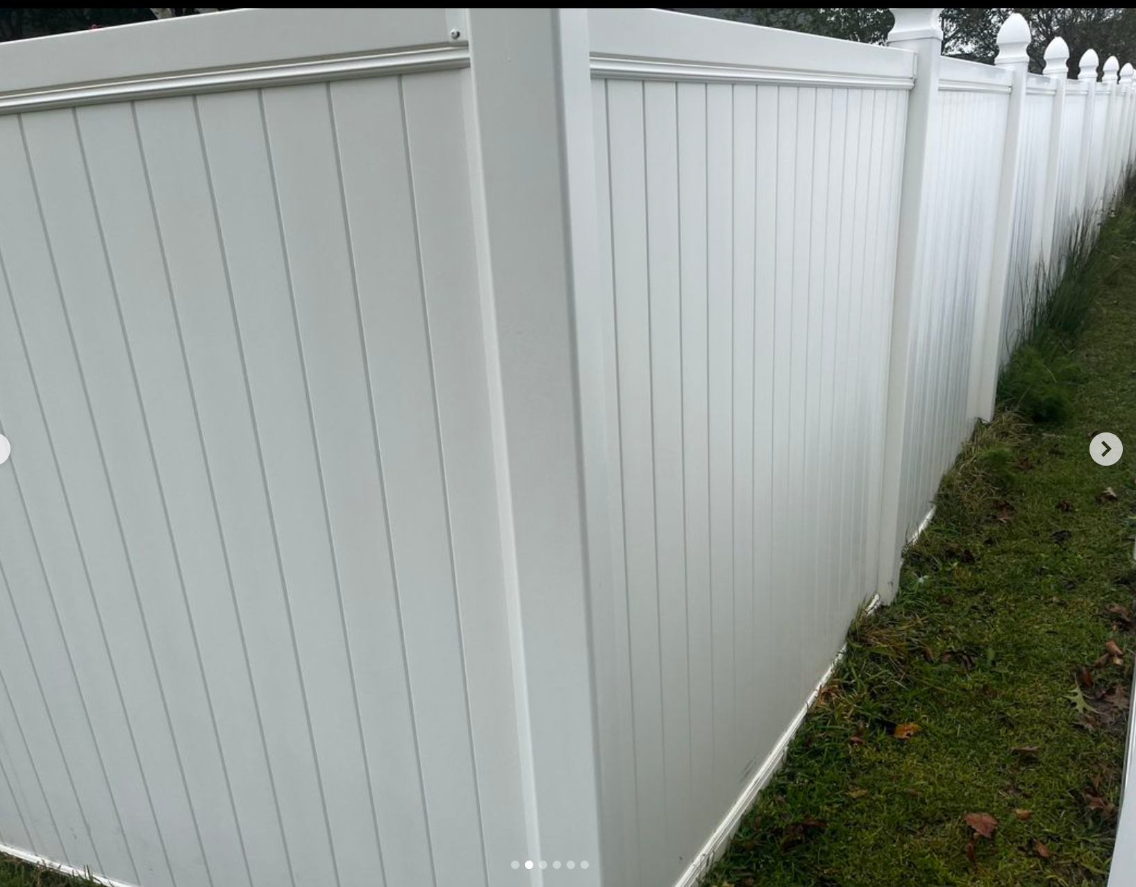 A white vinyl fence is sitting on top of a lush green field.