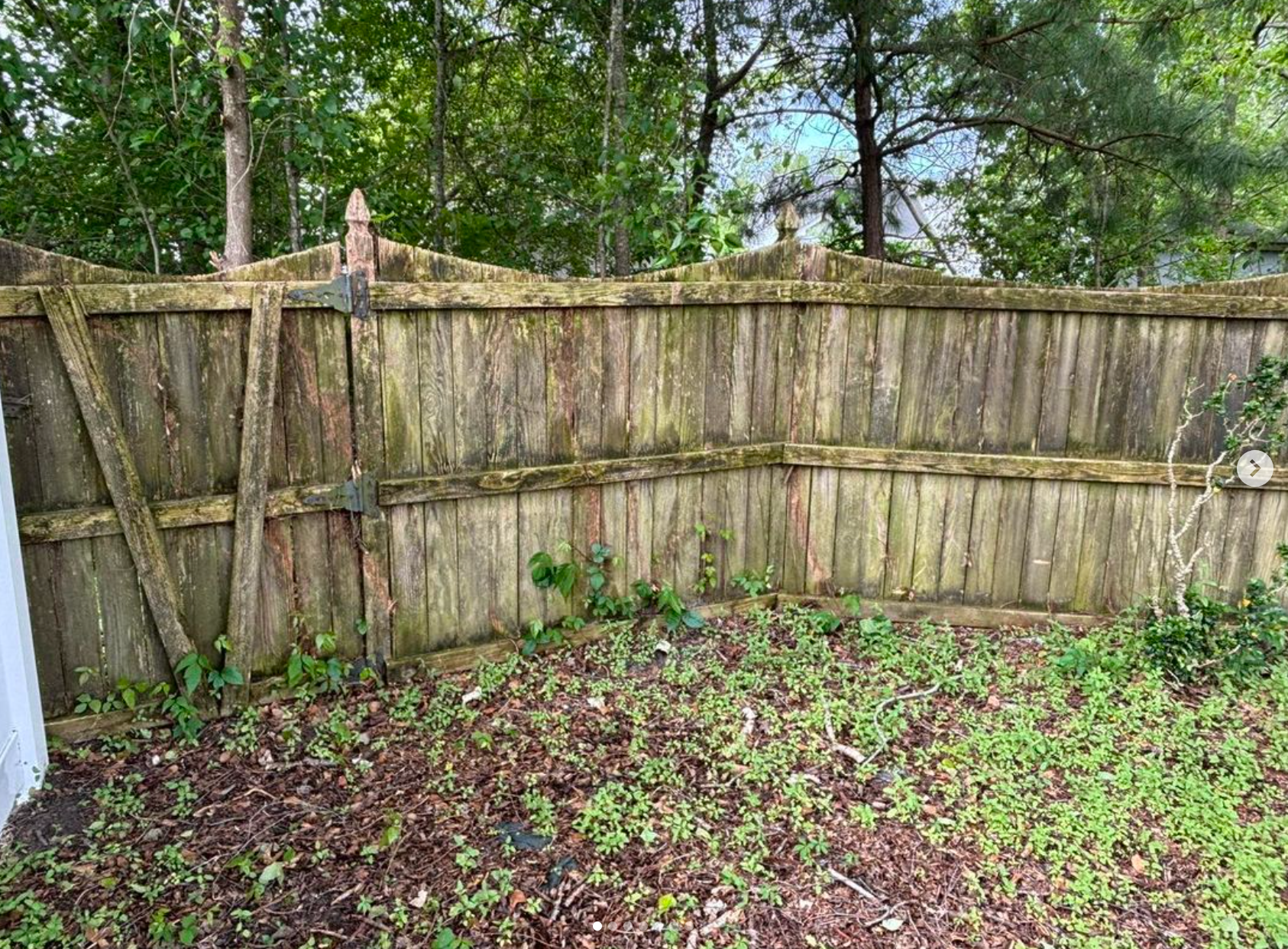 A wooden fence is sitting in the middle of a yard surrounded by trees.