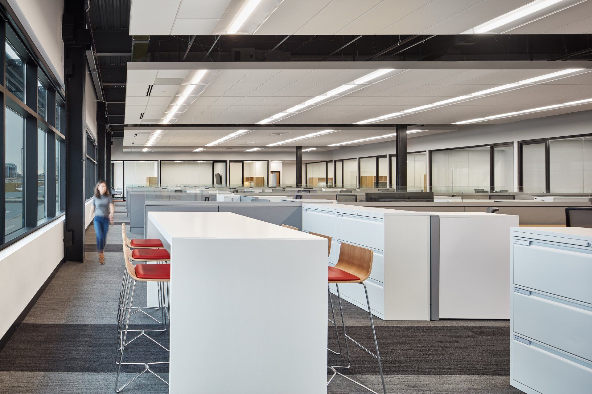 A woman is walking through an office with a long table and chairs.