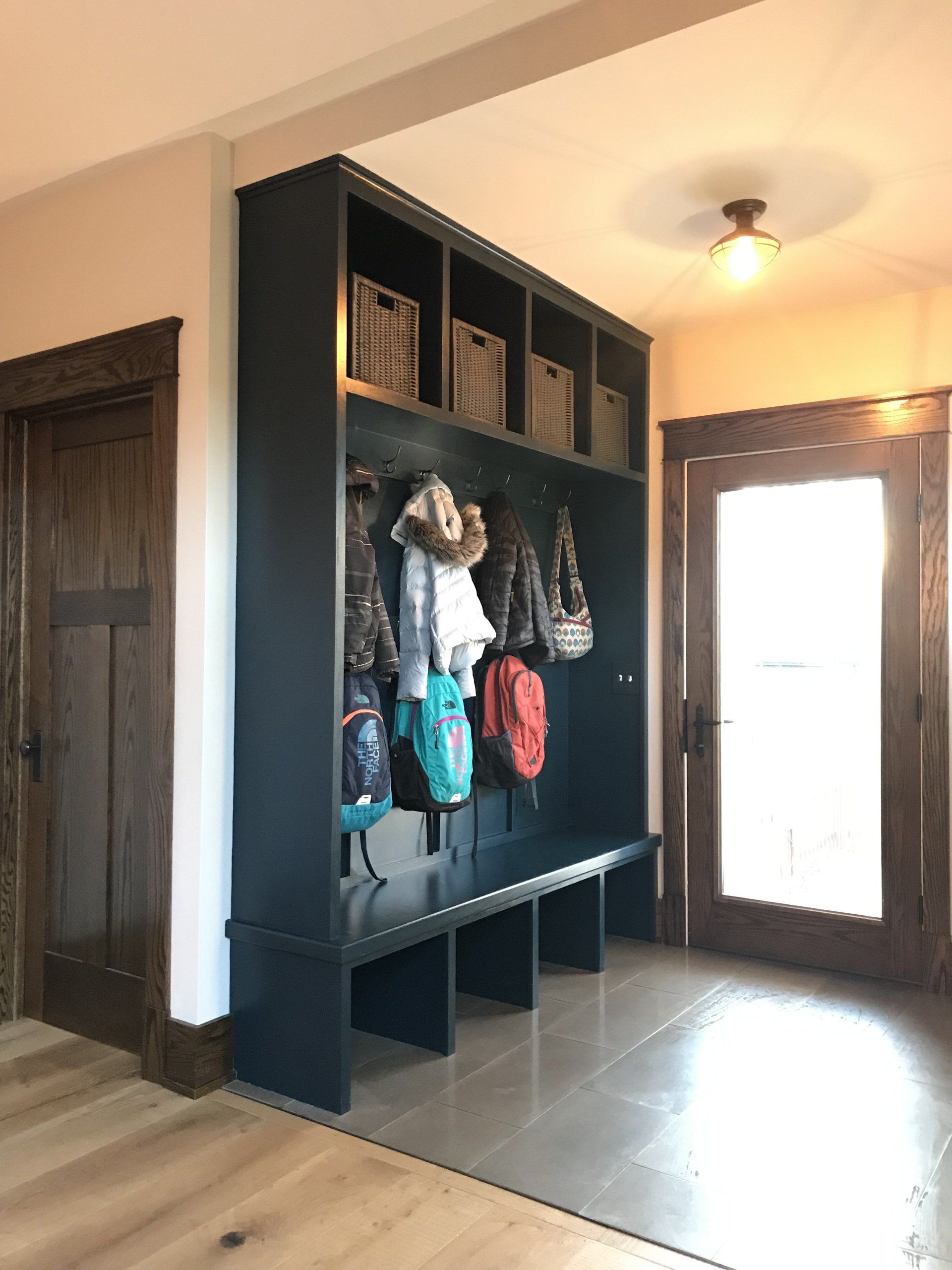 A hallway with a bench and a shelf filled with clothes and backpacks.