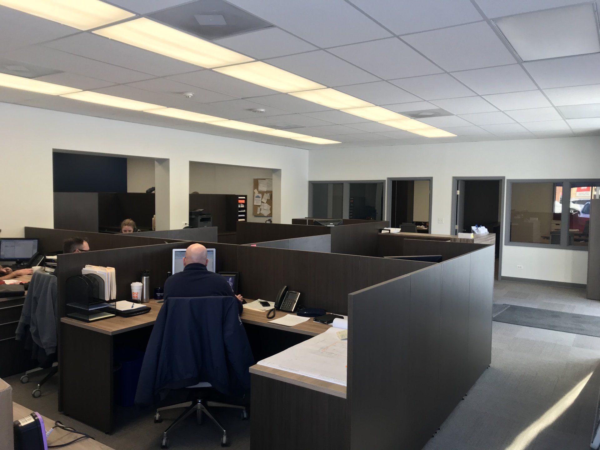 A man is sitting at a desk in a cubicle in an office.