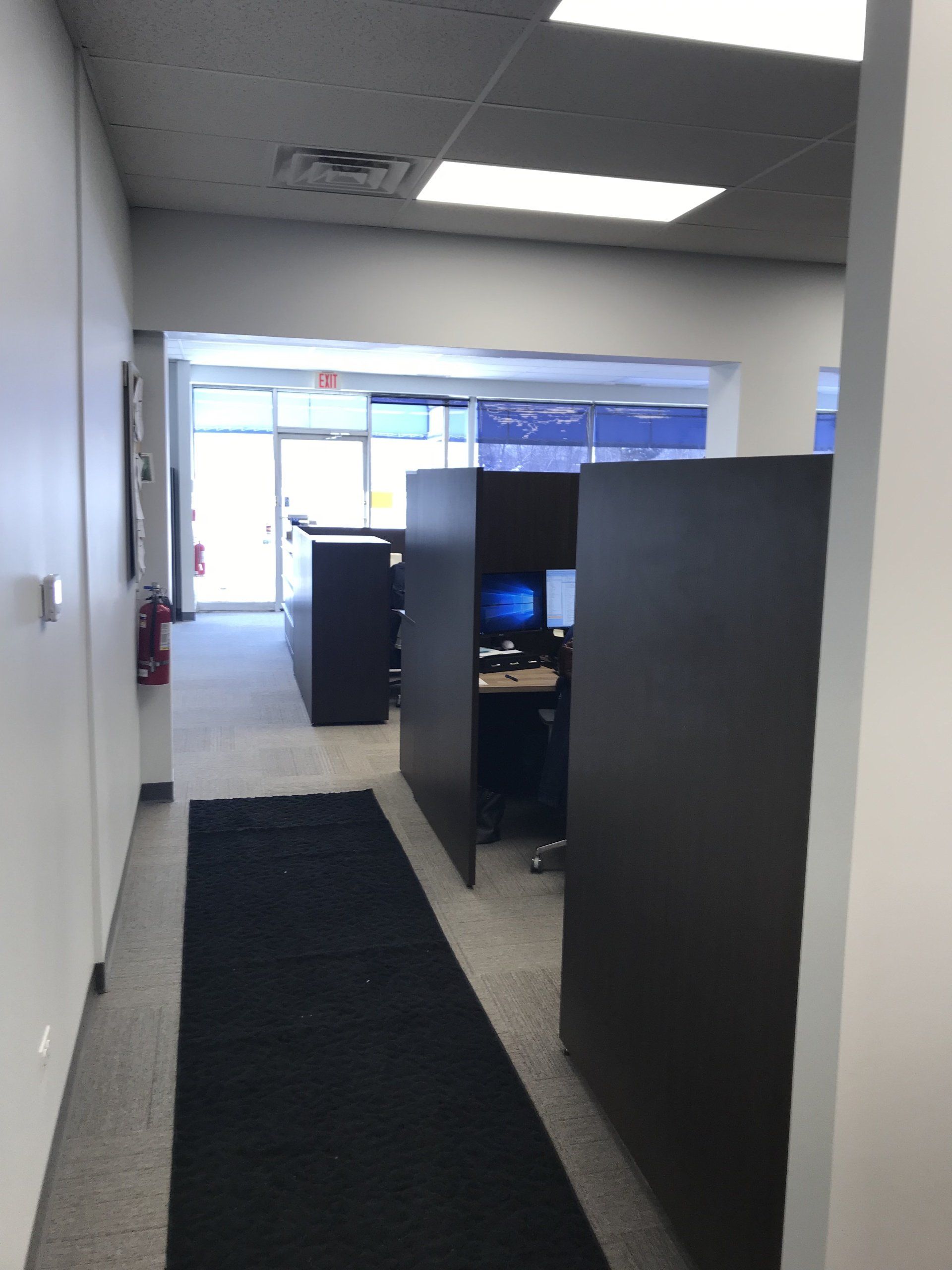 A hallway in an office with cubicles and a black rug