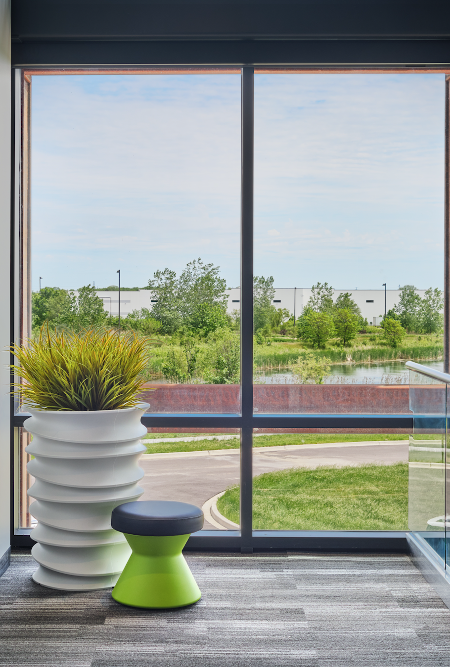 A room with a large window and a green stool in front of it.