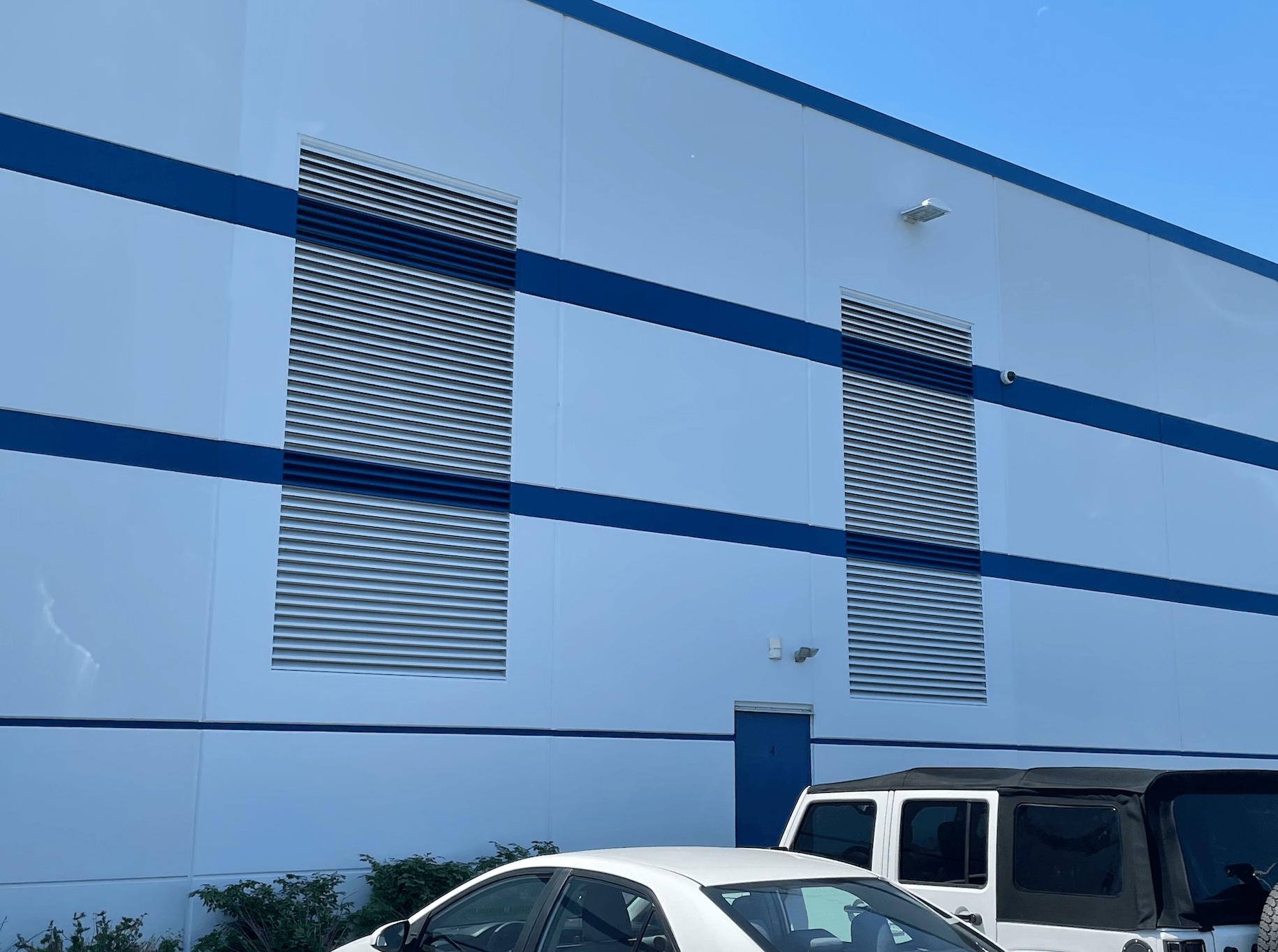 A white car is parked in front of a building with blue stripes