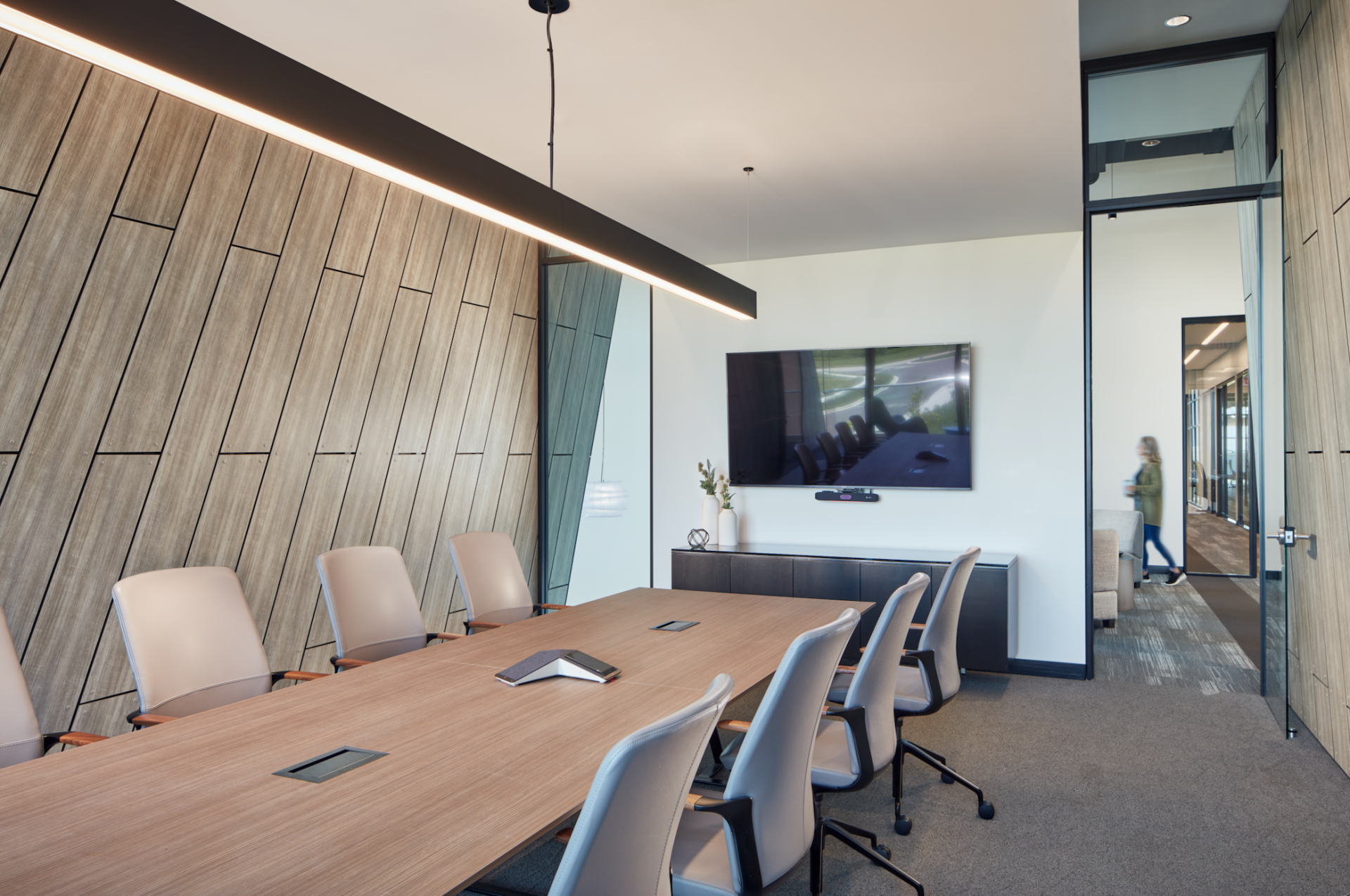 A conference room with a long wooden table and chairs and a flat screen tv on the wall.