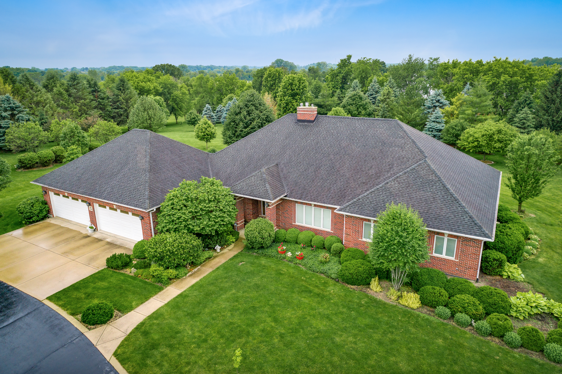 An aerial view of a large brick house with a black roof surrounded by trees and grass.