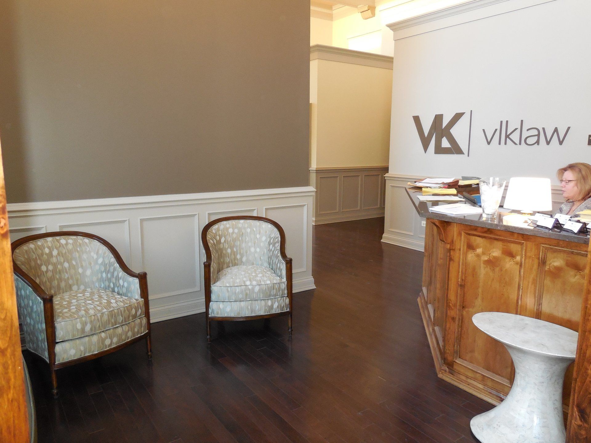 A woman is sitting at a desk in a waiting room with chairs.
