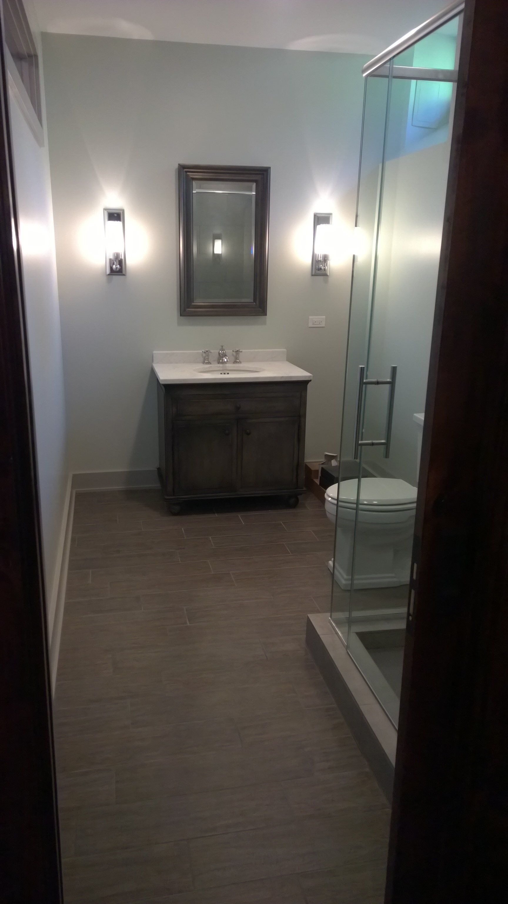 A bathroom with a sink , toilet , mirror and walk in shower.