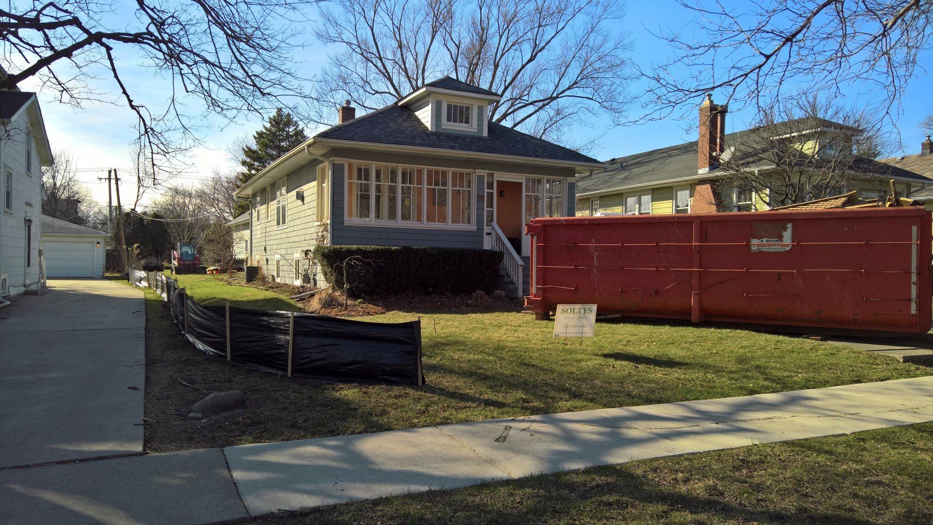 A large red dumpster is parked in front of a house.