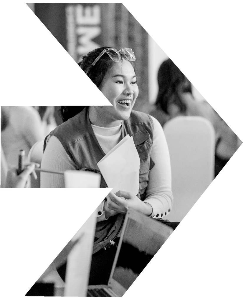 A black and white photo of a woman sitting at a table holding a piece of paper.