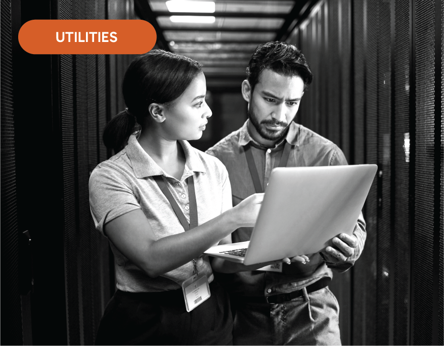 A man and a woman are looking at a laptop in a server room.