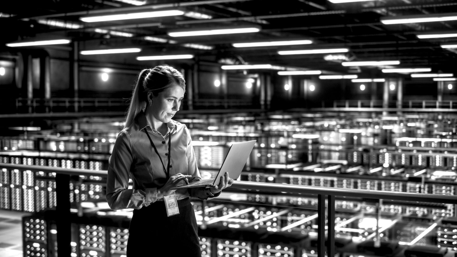 A woman is standing in a warehouse looking at a laptop computer.