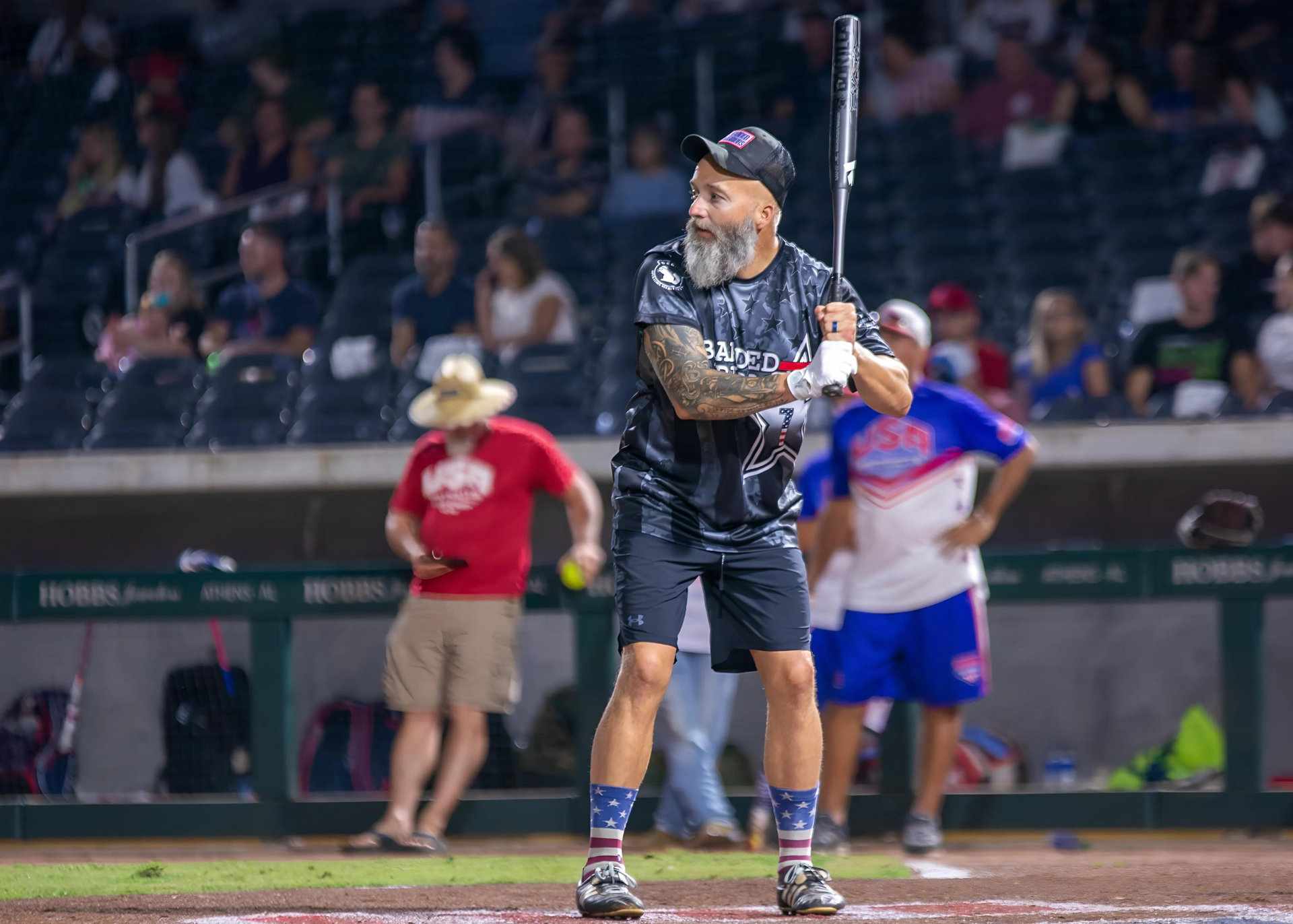 A man with a beard is holding a baseball bat on a baseball field.