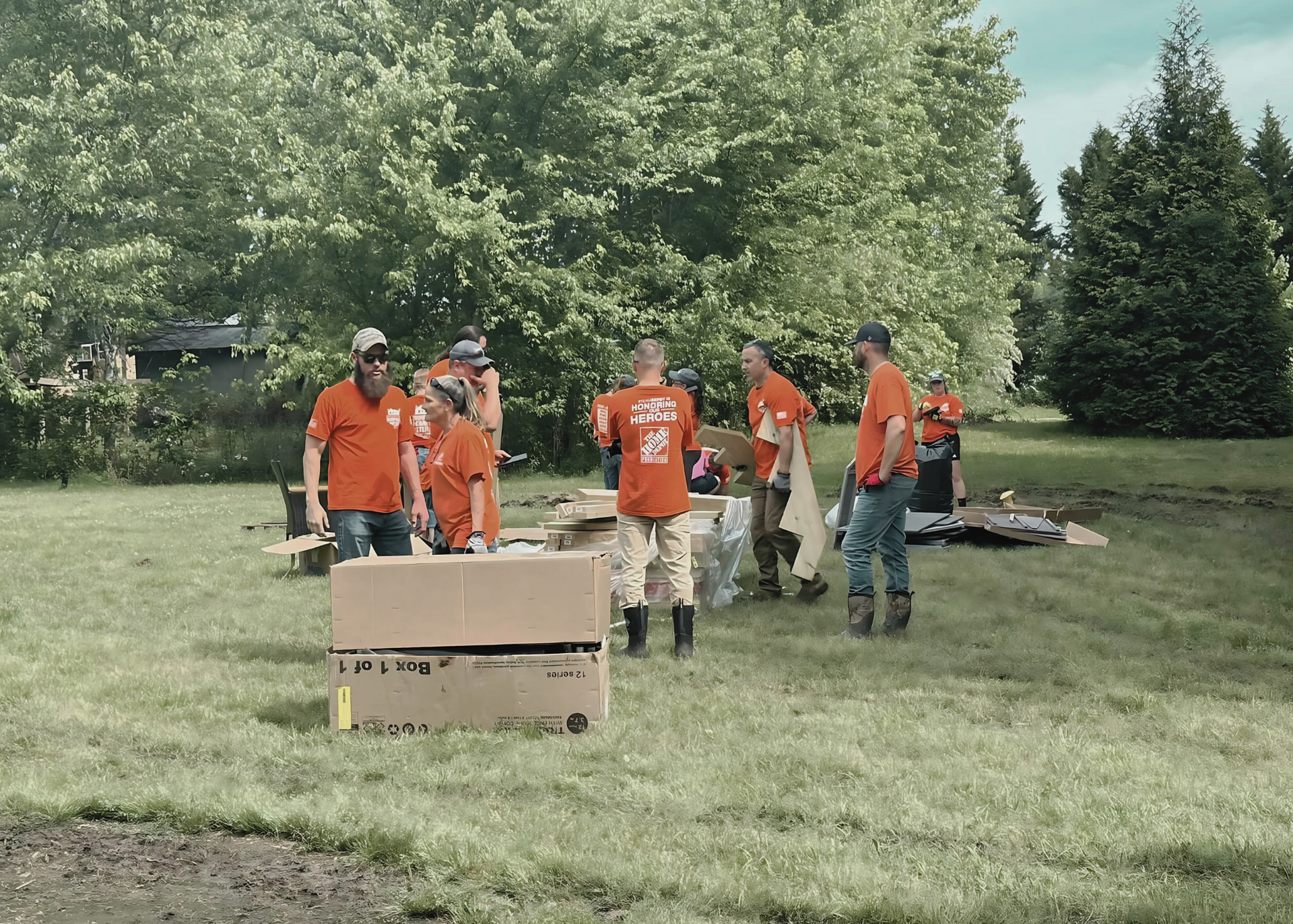 A group of people in orange shirts are standing in a grassy field