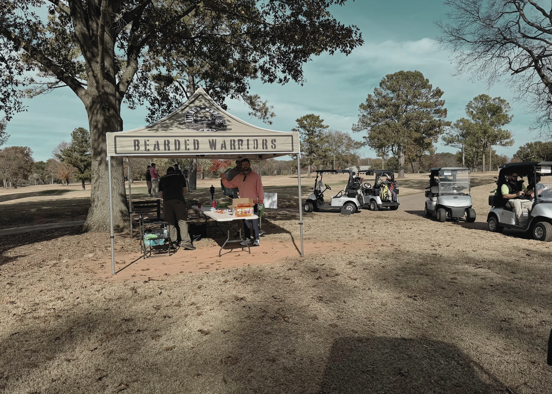 A group of golf carts are parked under a canopy that says beard & barbeque