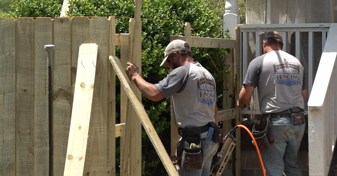Two men are working on a wooden fence.
