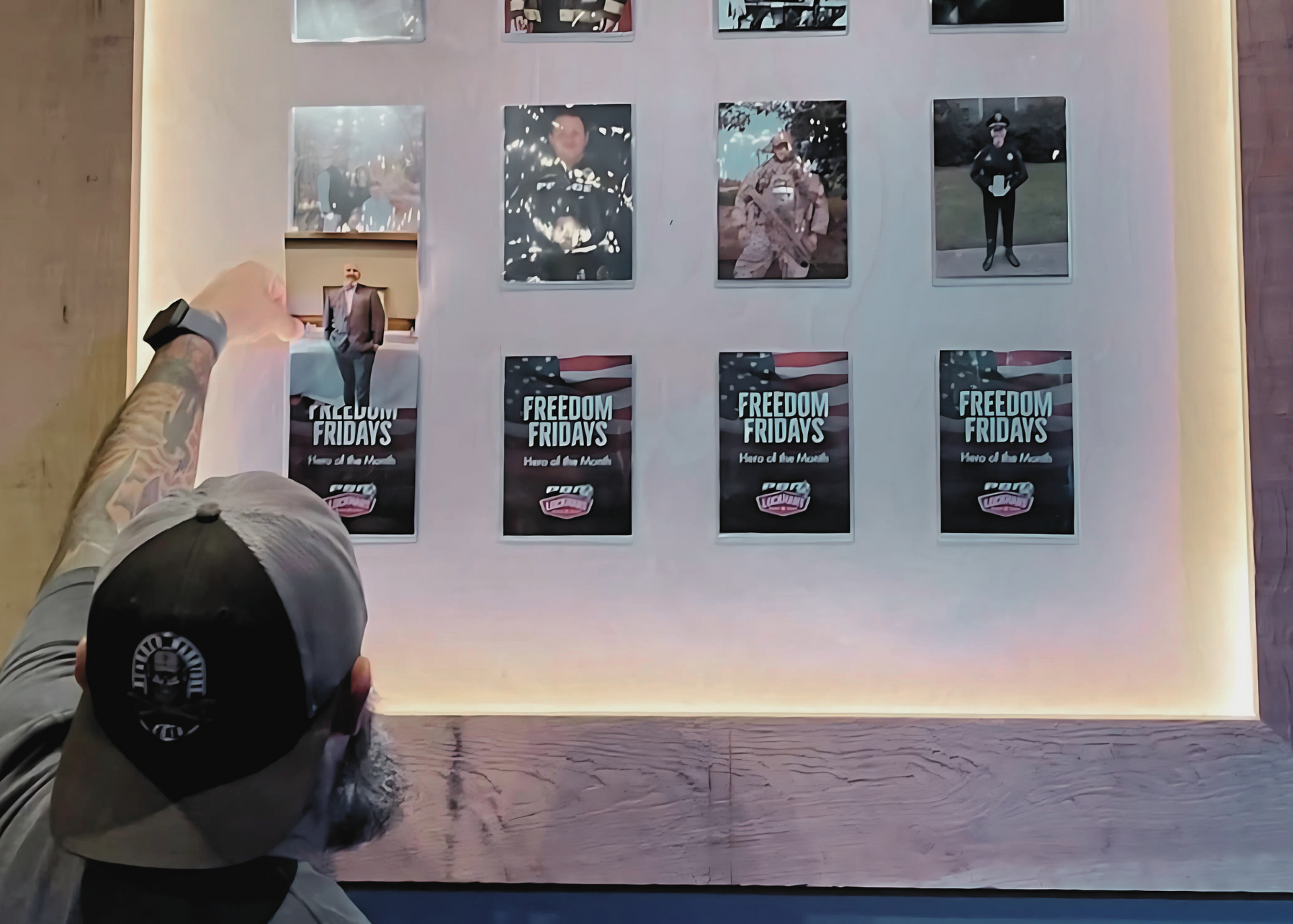 A man in a baseball cap is pointing at a wall with pictures on it