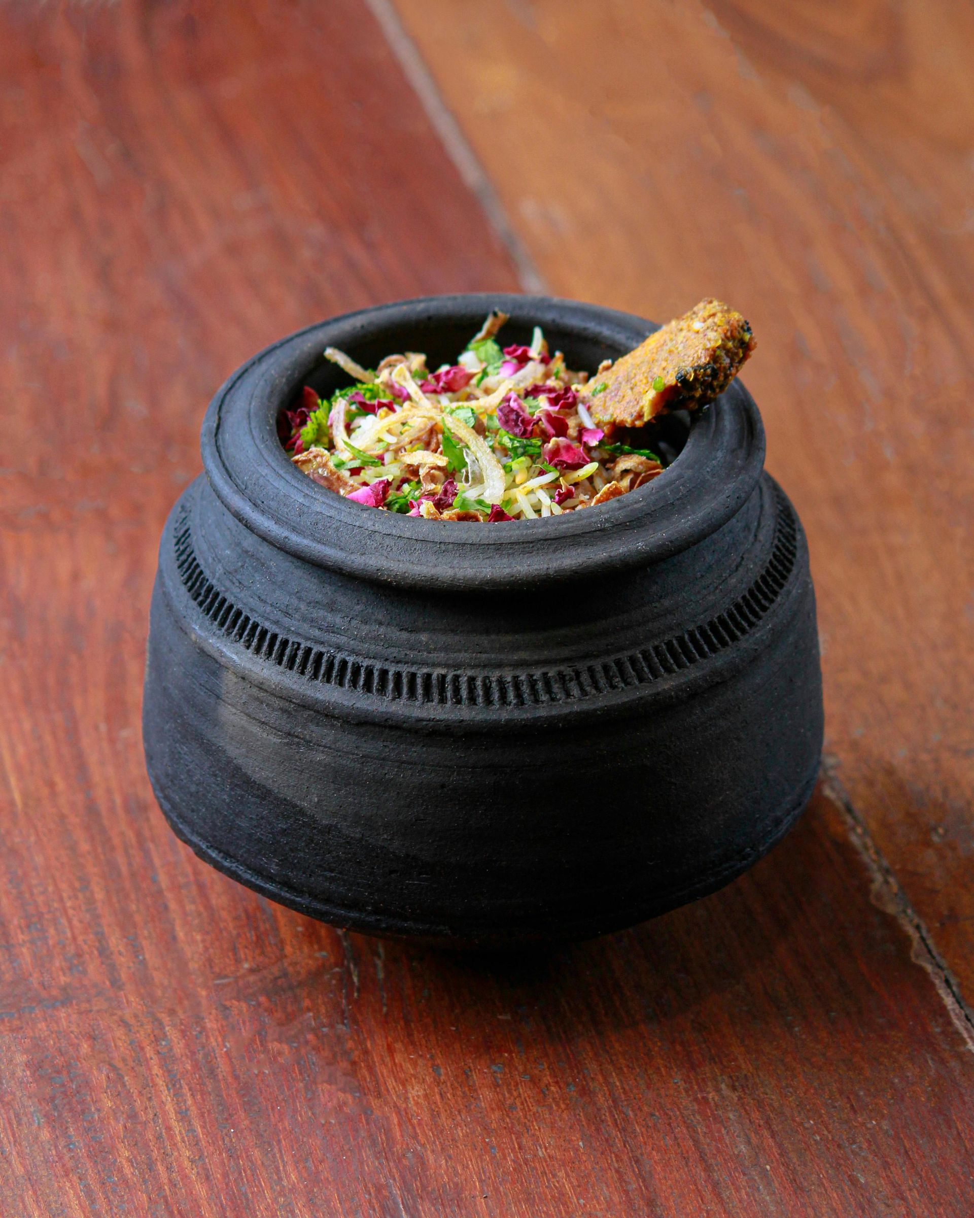 Small black pot of food on a wooden surface, with a crispy bread garnish.