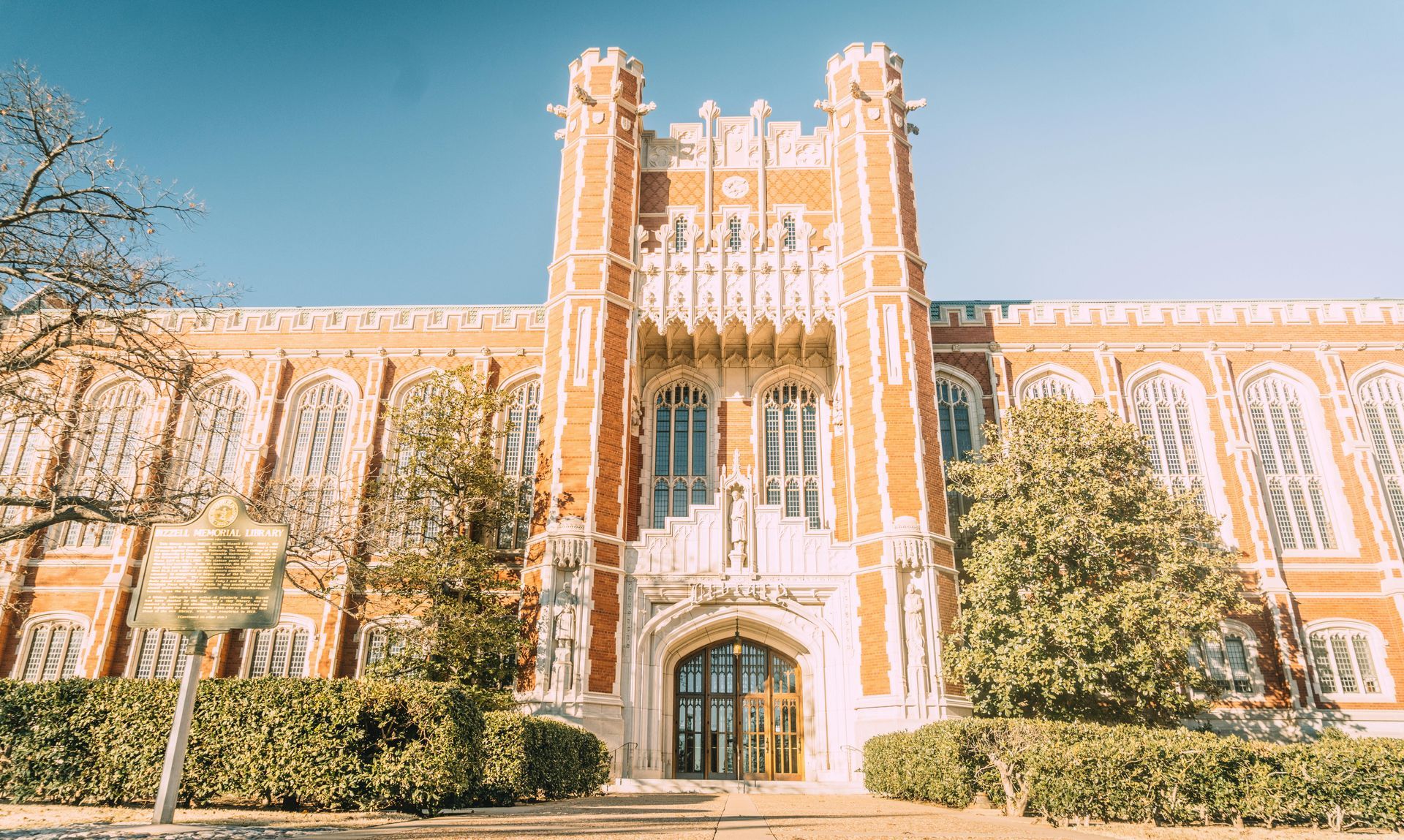 Brick university building with ornate details and arched windows under a blue sky.