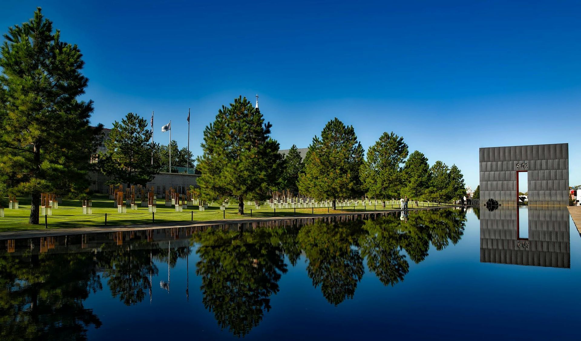 Oklahoma City National Memorial and Museum, reflecting pool with trees and monument under blue sky.