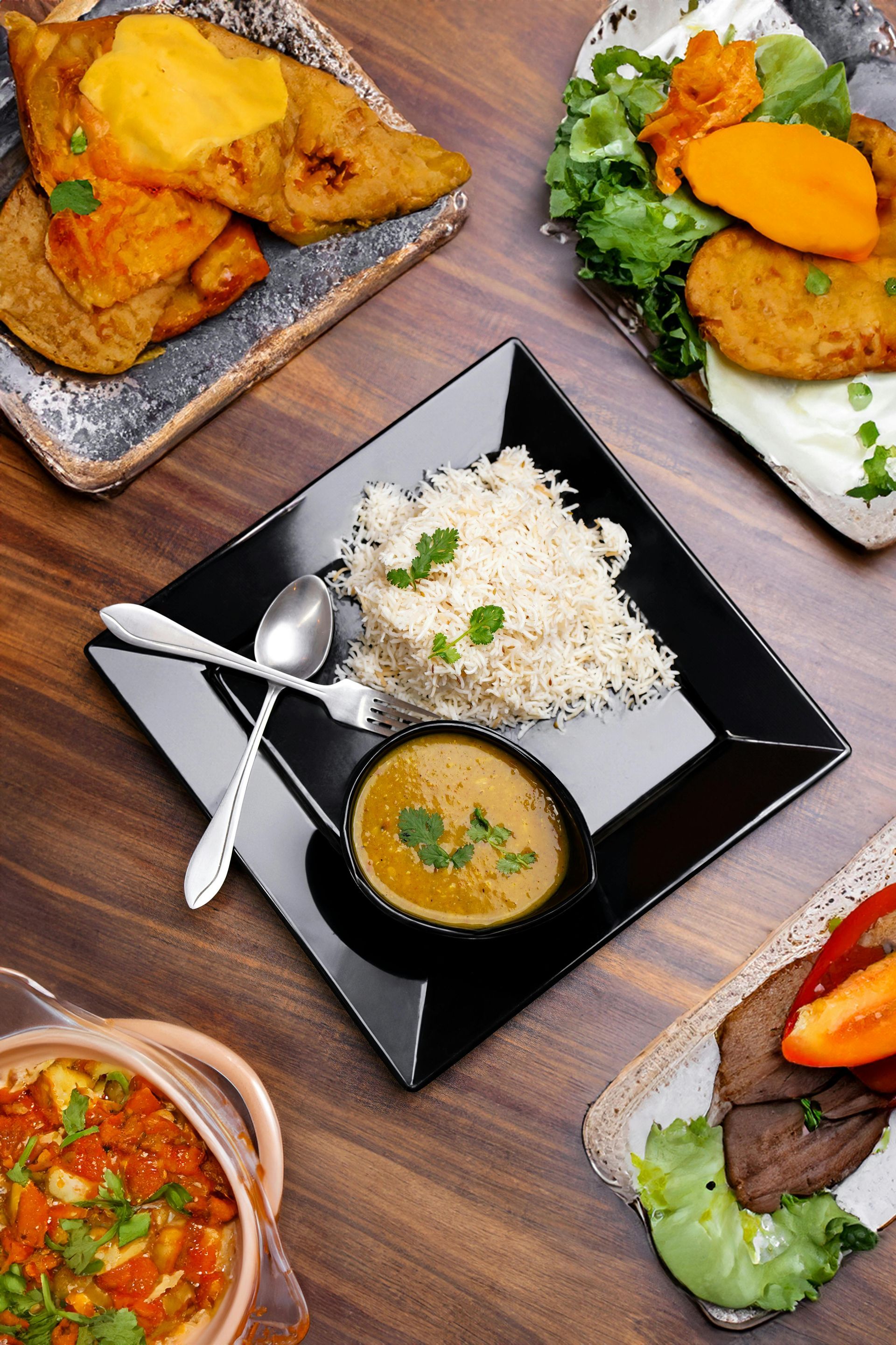 Several plates of food on a wooden table, including rice, curry, and fried items.
