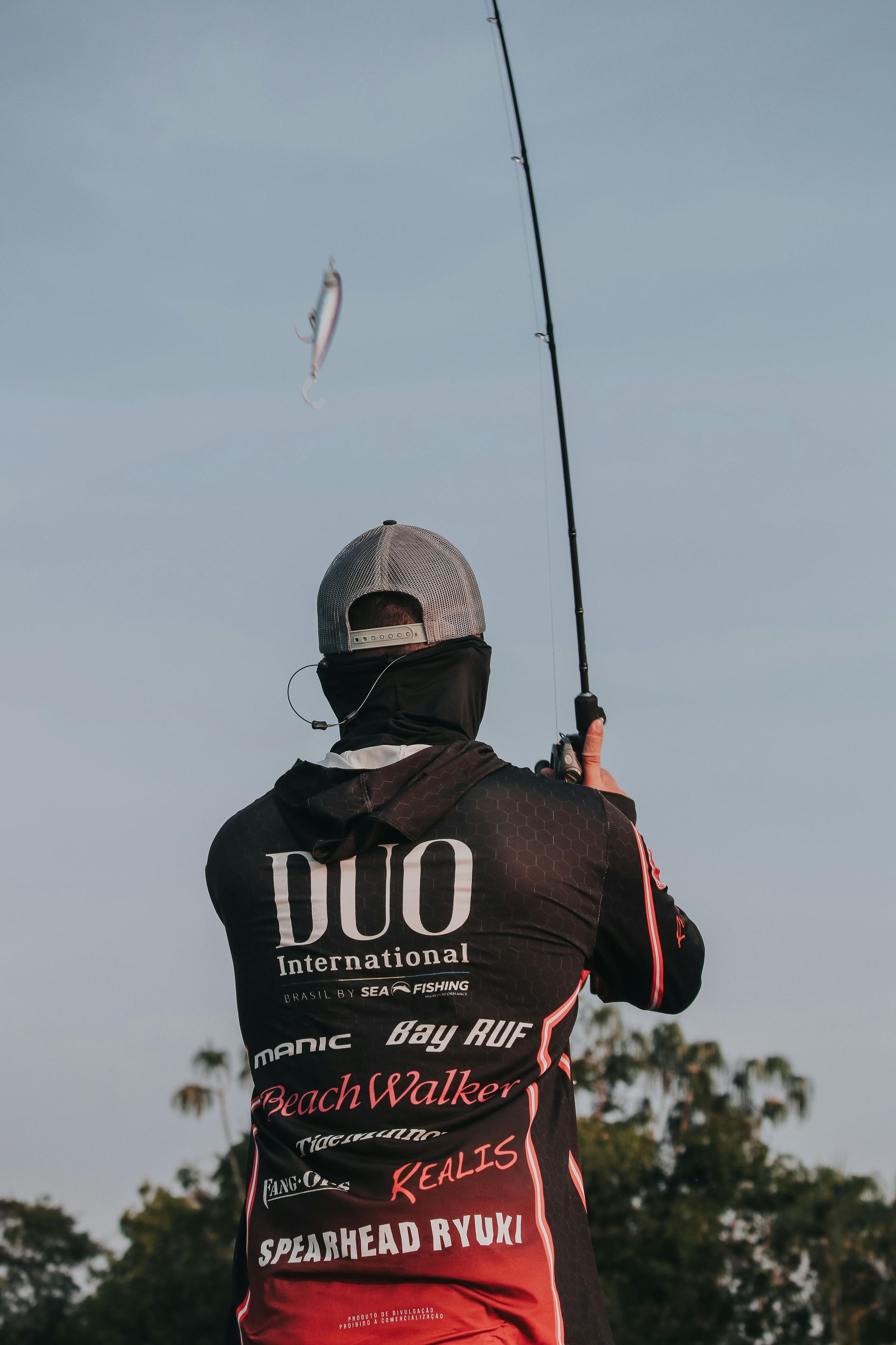 Fisherman casting a lure with a fishing rod outdoors, against a blue sky.