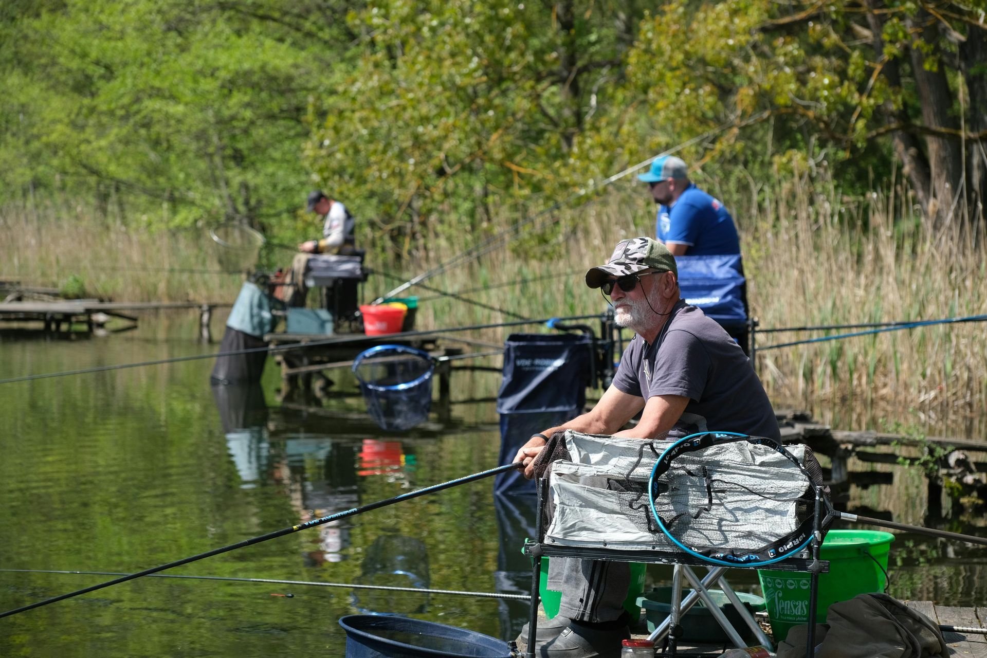 People fishing from platforms on a lake, surrounded by greenery.