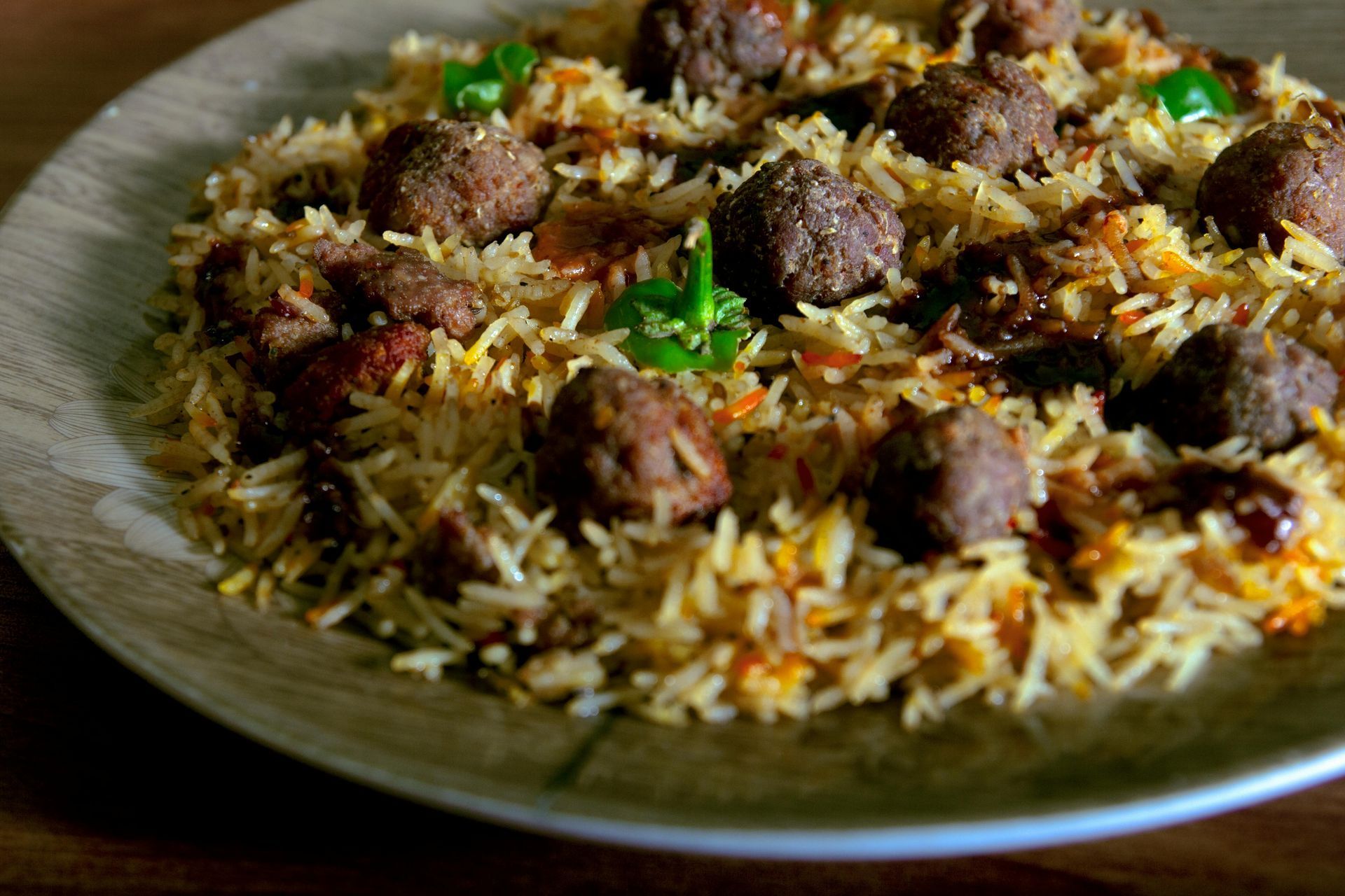 Rice pilaf topped with meat balls, garnished with green chilies, served on a wooden plate.