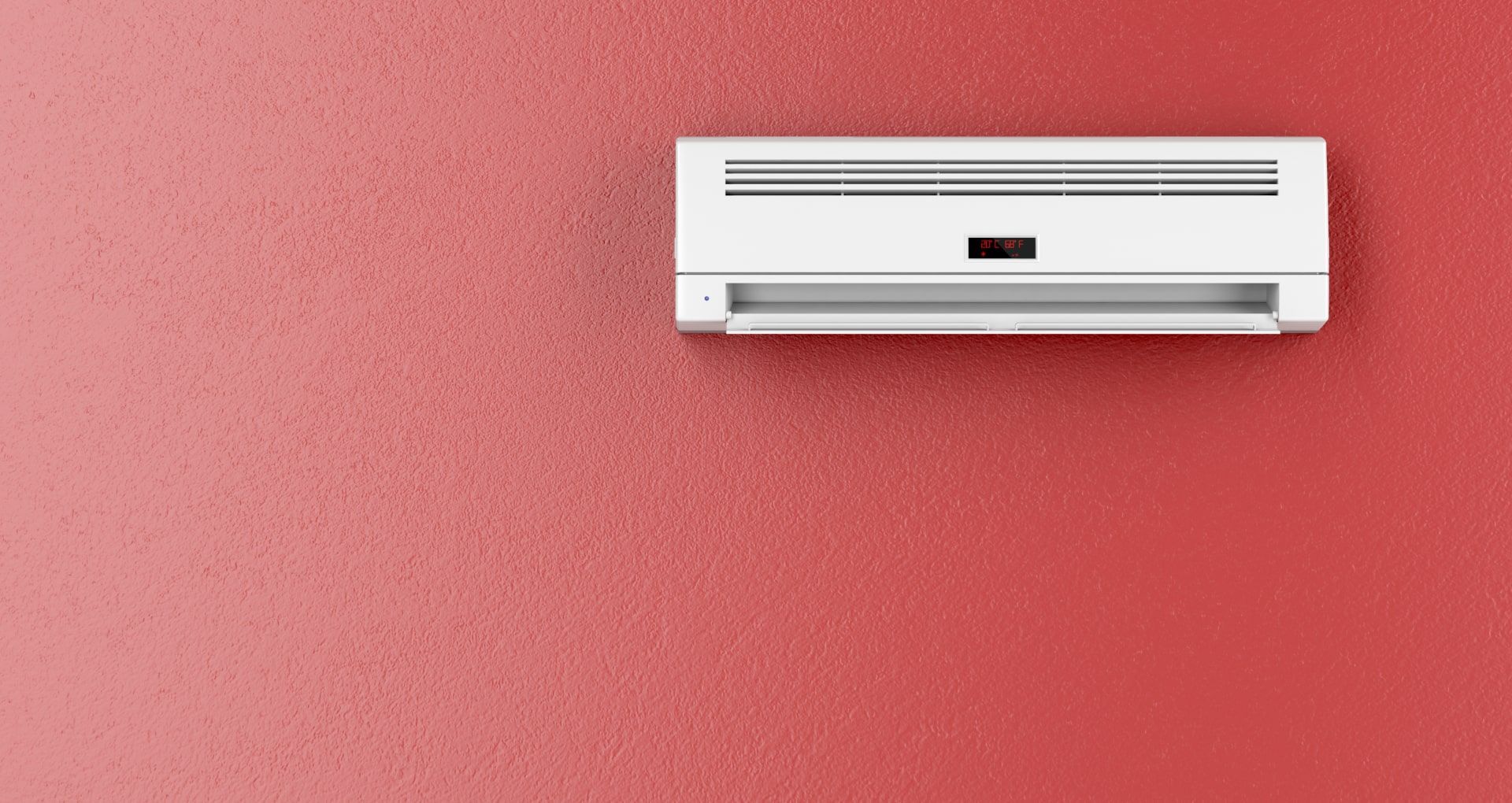 A white air conditioner is mounted on a red wall.