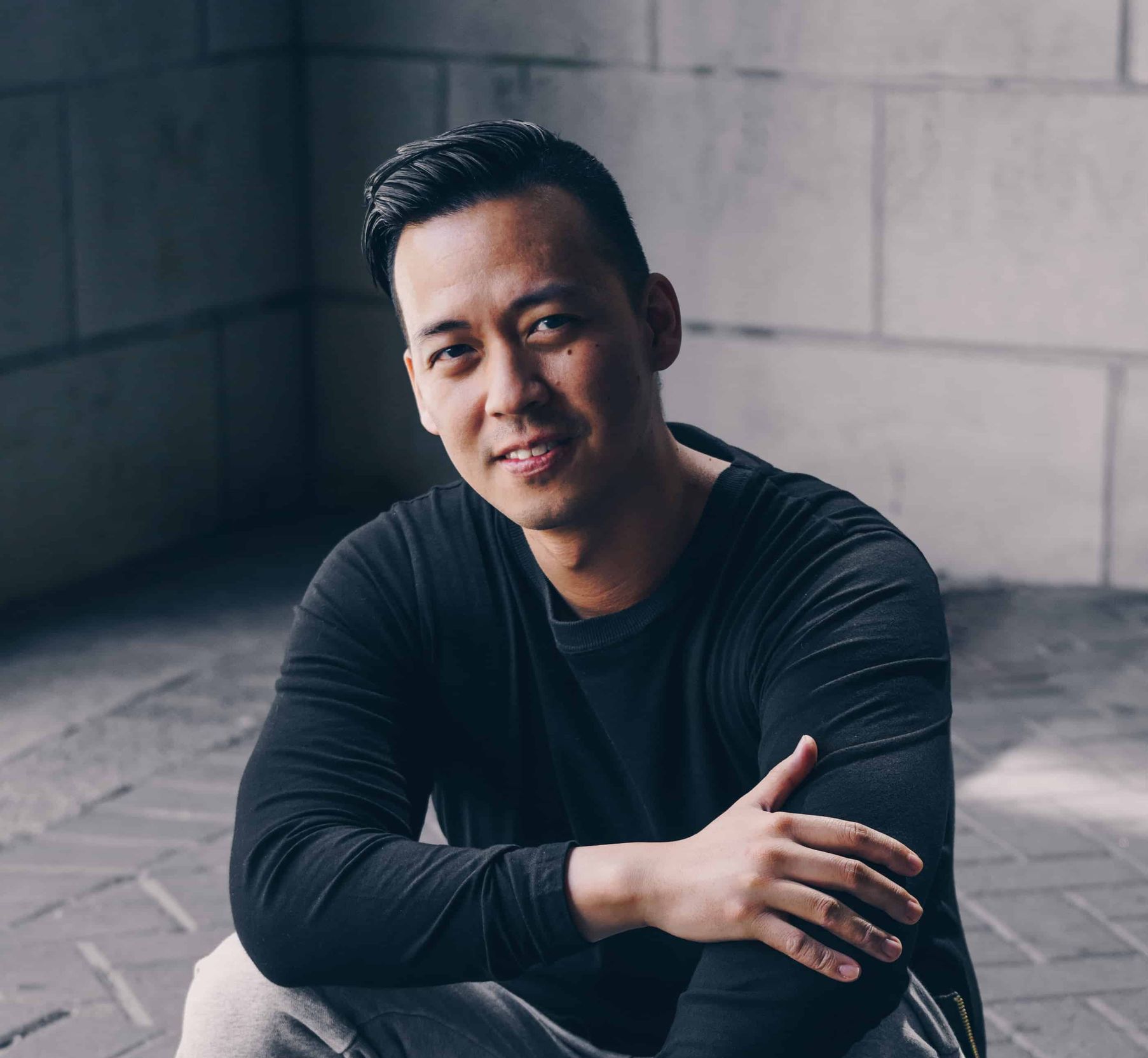 A man in a black shirt is sitting on the ground with his arms crossed.