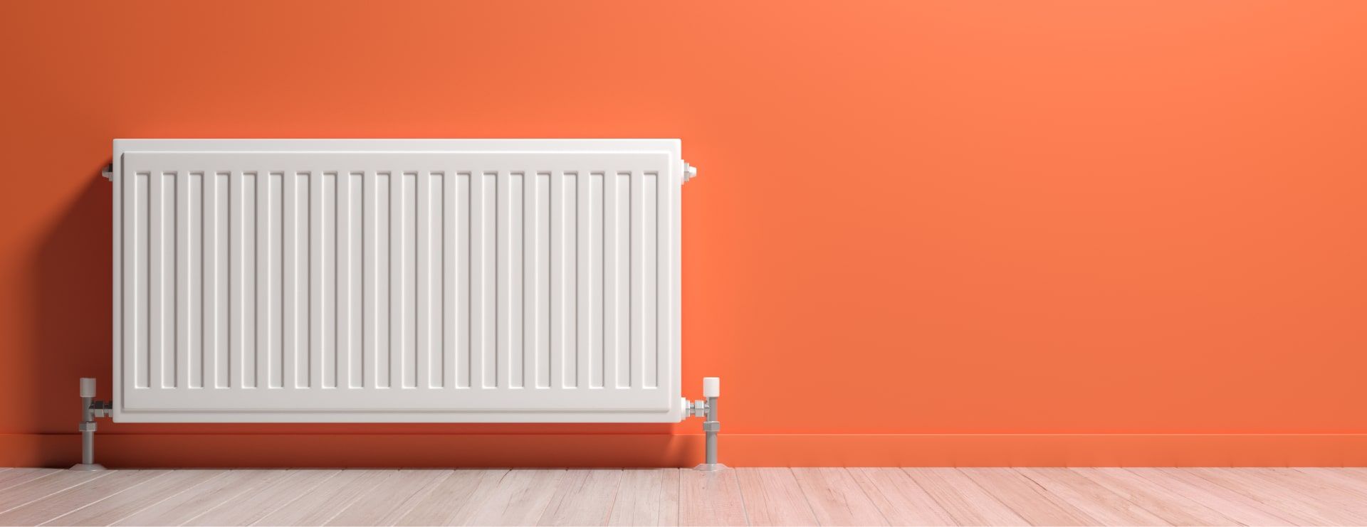 A white radiator is sitting in front of an orange wall.