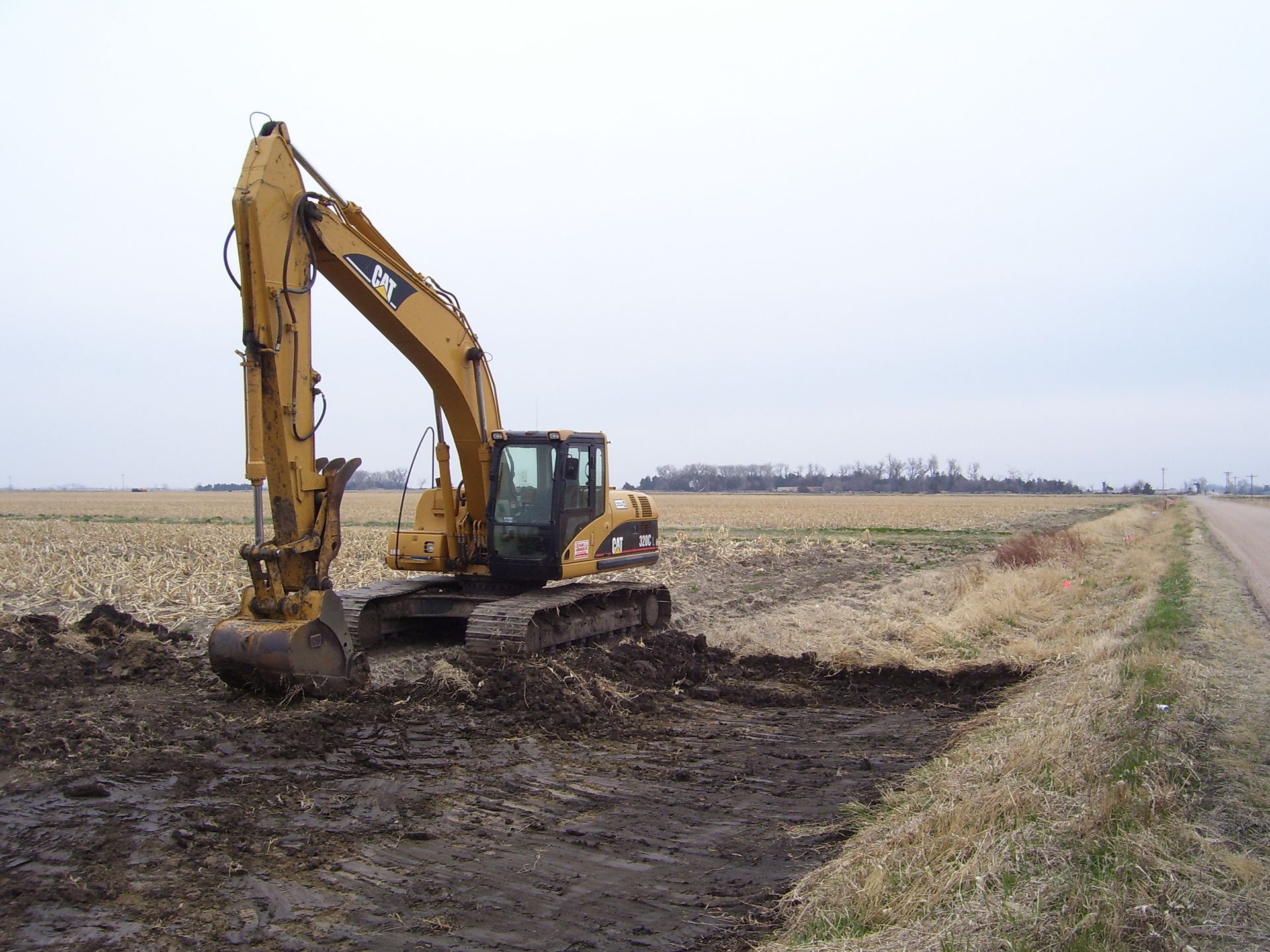 A yellow excavator is digging a hole in a field