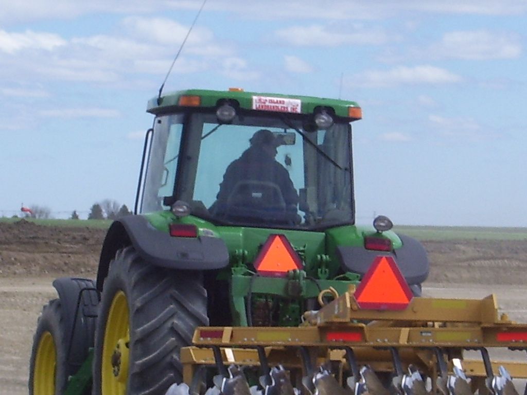 A green john deere tractor is plowing a field