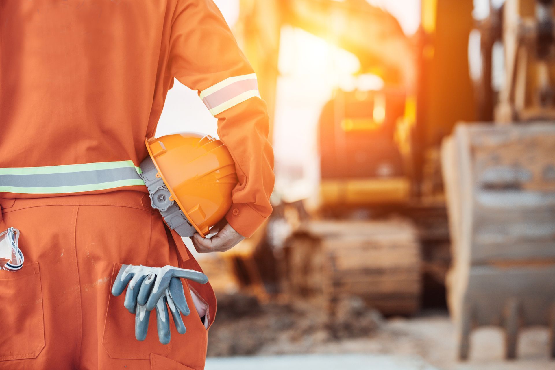 A construction worker is holding a hard hat and gloves at a construction site.