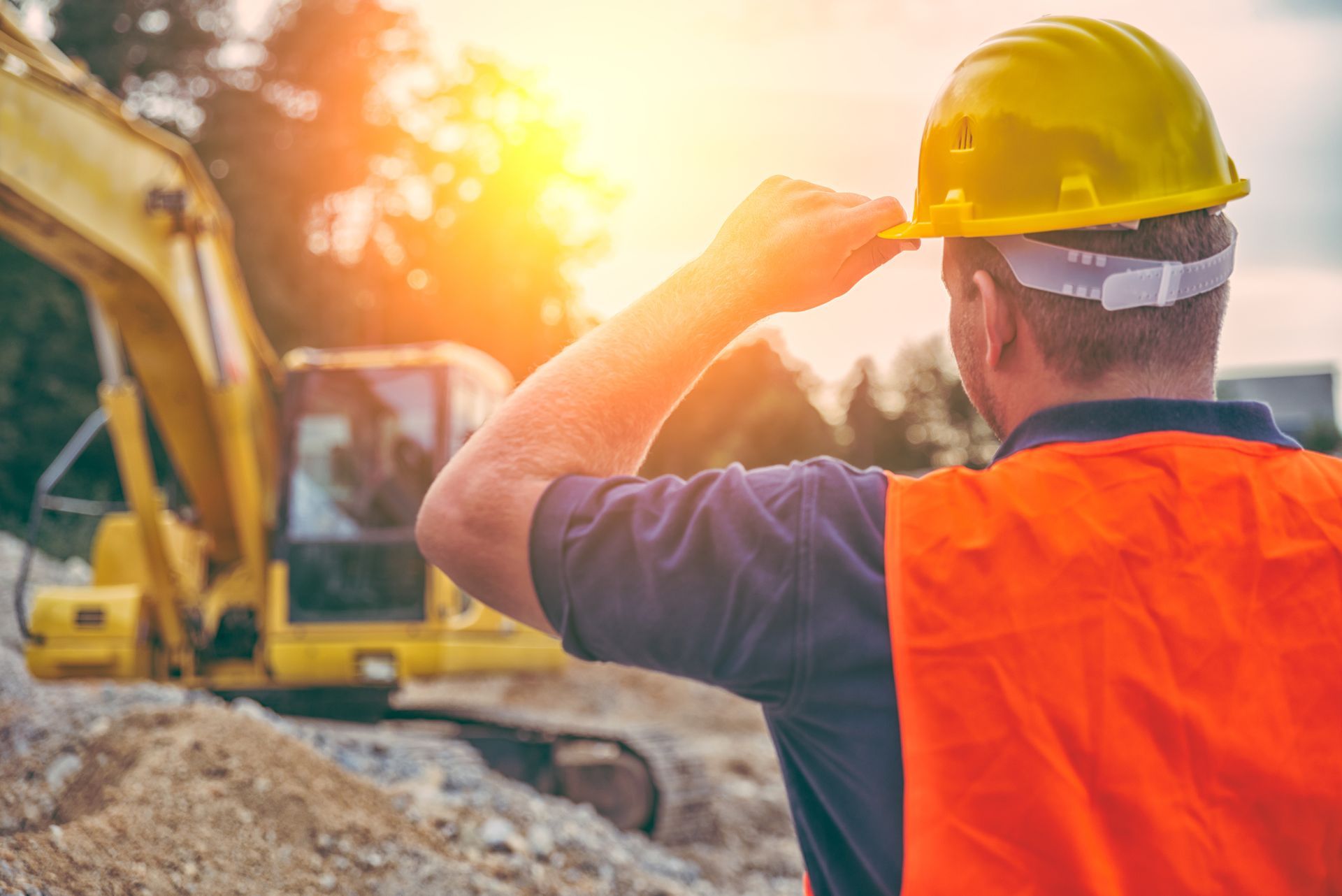A construction worker wearing a hard hat and safety vest is looking at a bulldozer on a construction site.