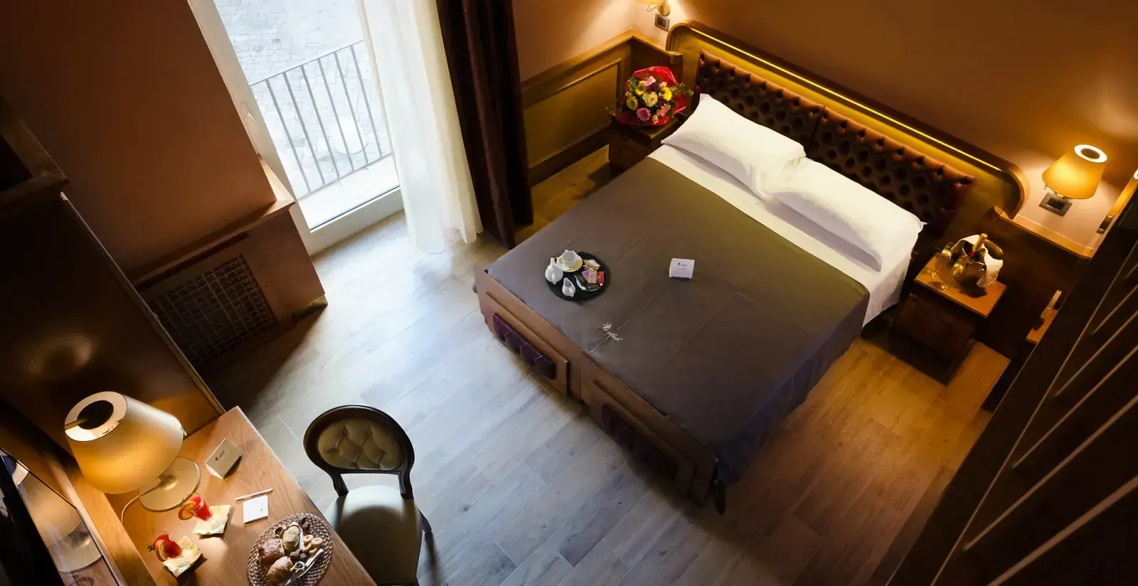 Accogliente camera d'albergo con letto, comodini e scrivania. Illuminazione calda e mobili in legno scuro.